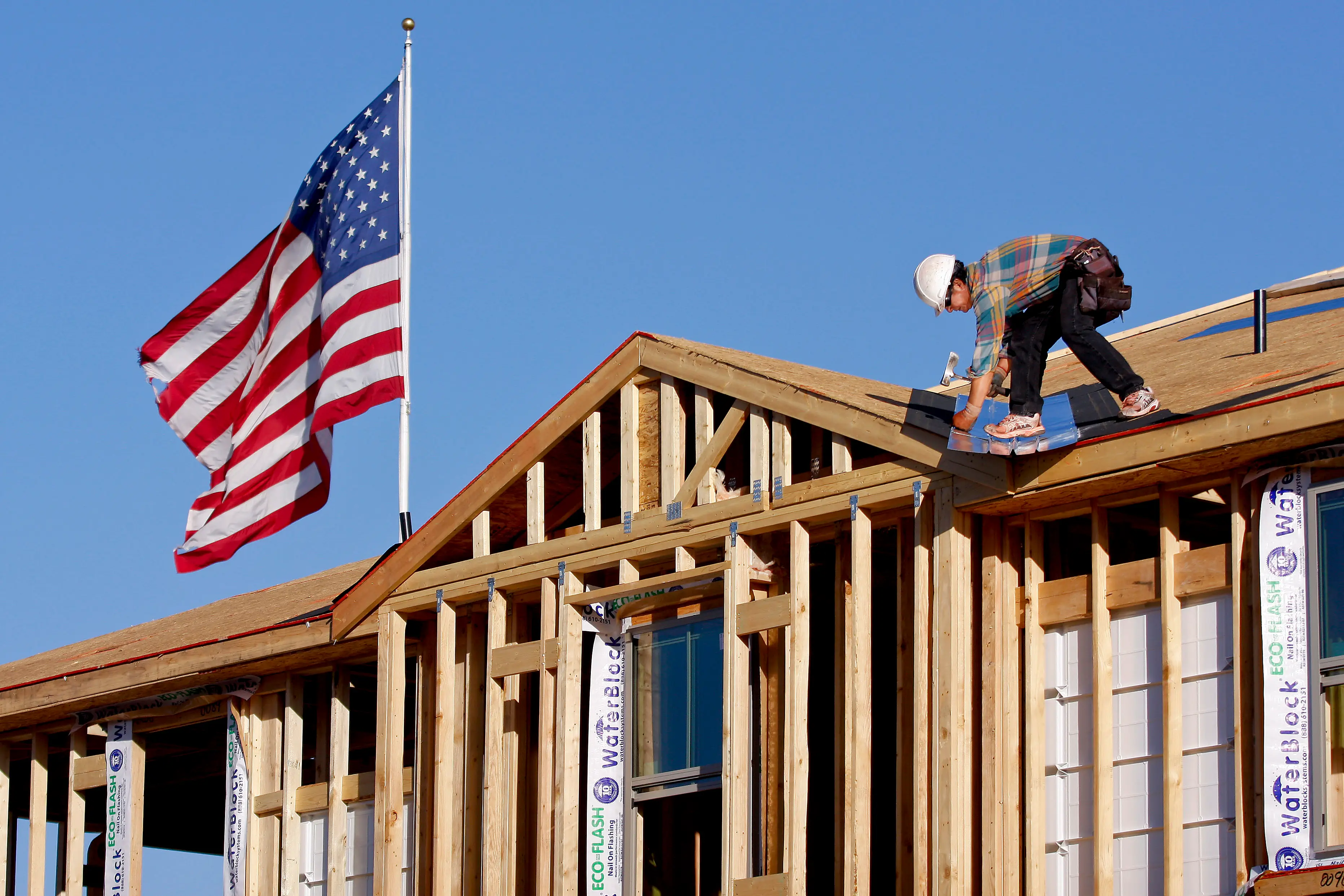Construction worker kneeling on the roof of a home in construction