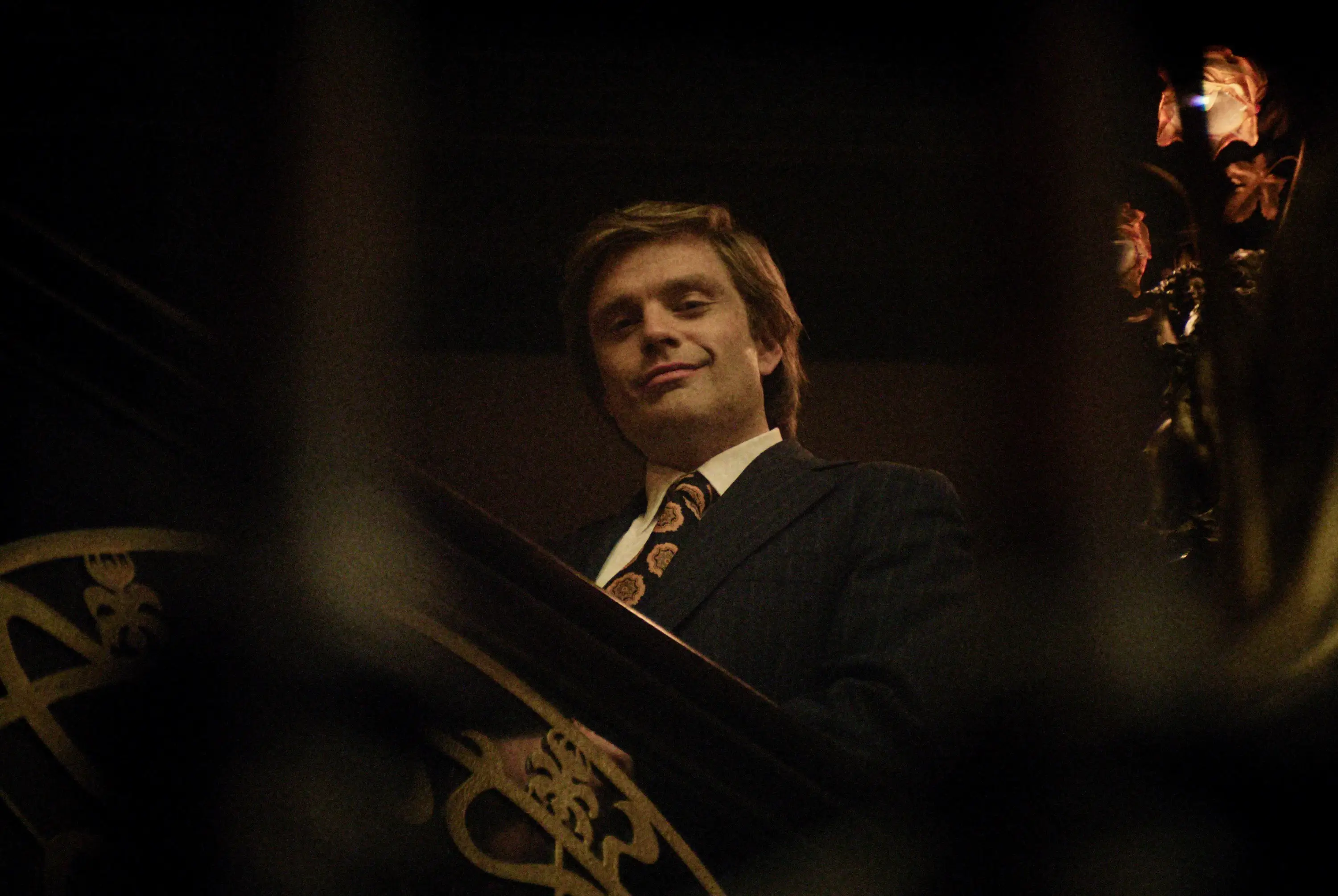 Sebastian Stan in a suit and tie smiling on a staircase in The Apprentice