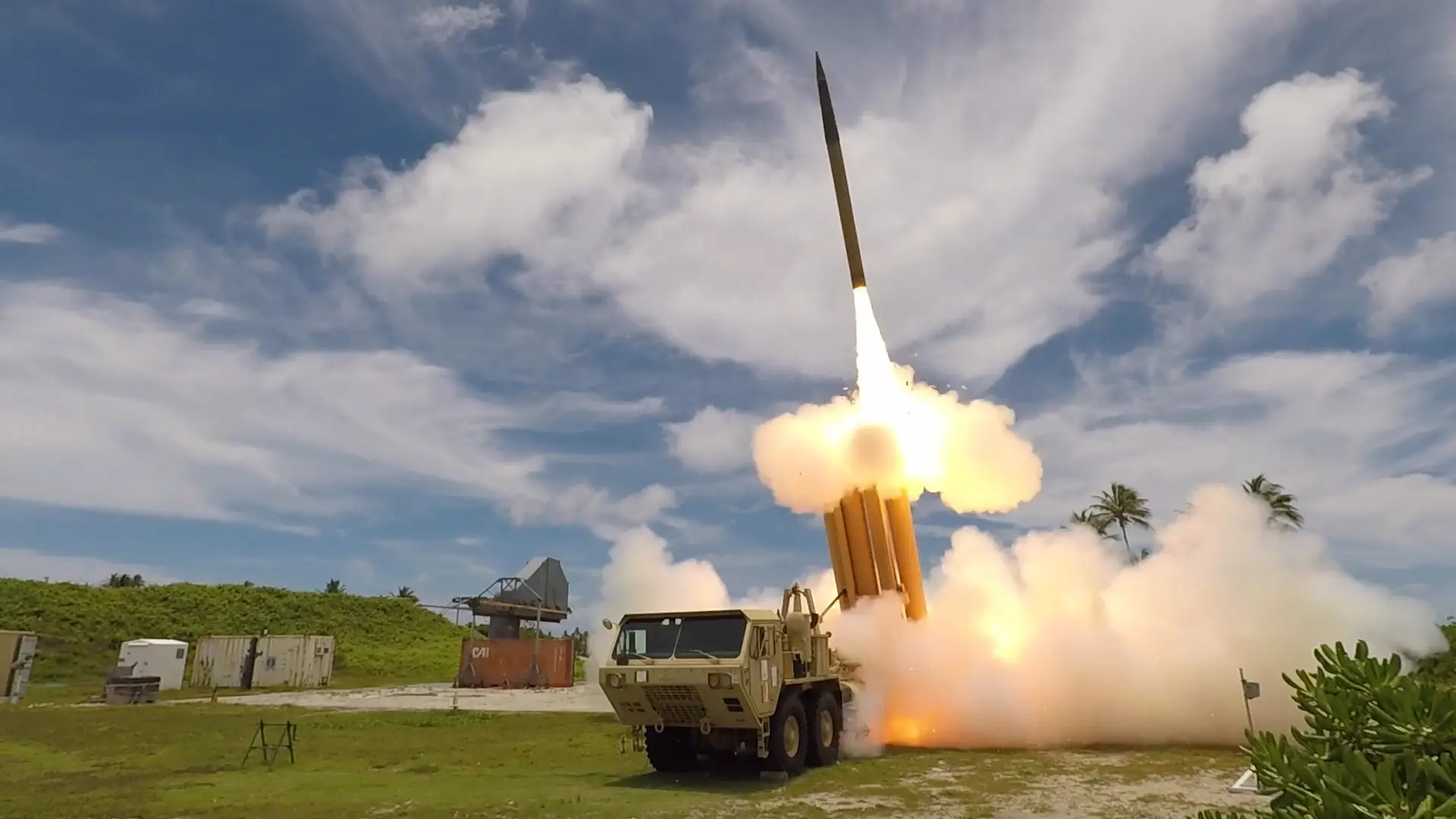 A THAAD interceptor is launched on an island test site into a cloudy blue sky.