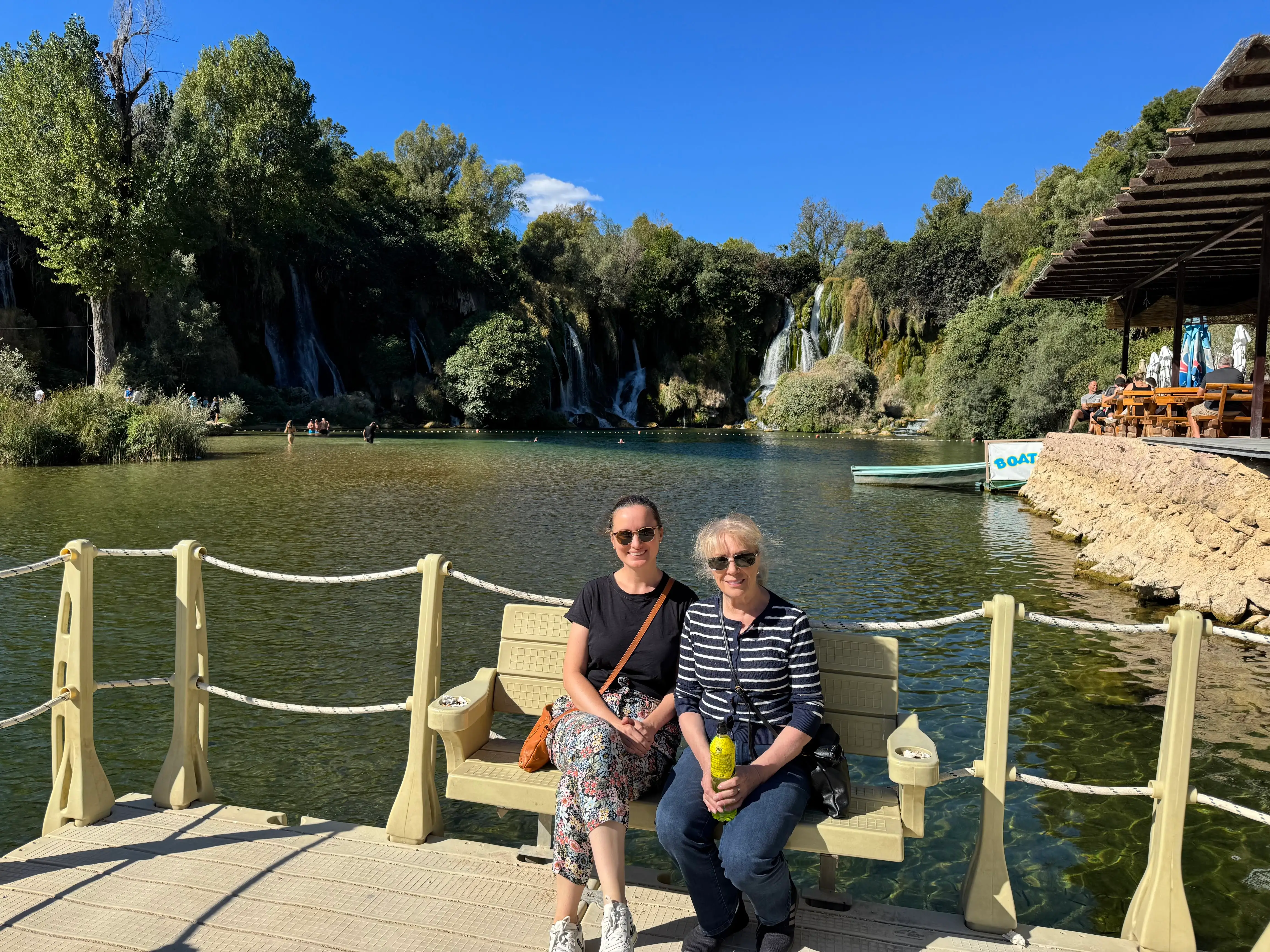 Agnes and her mom sitting on a bench near a lake with a waterfall.