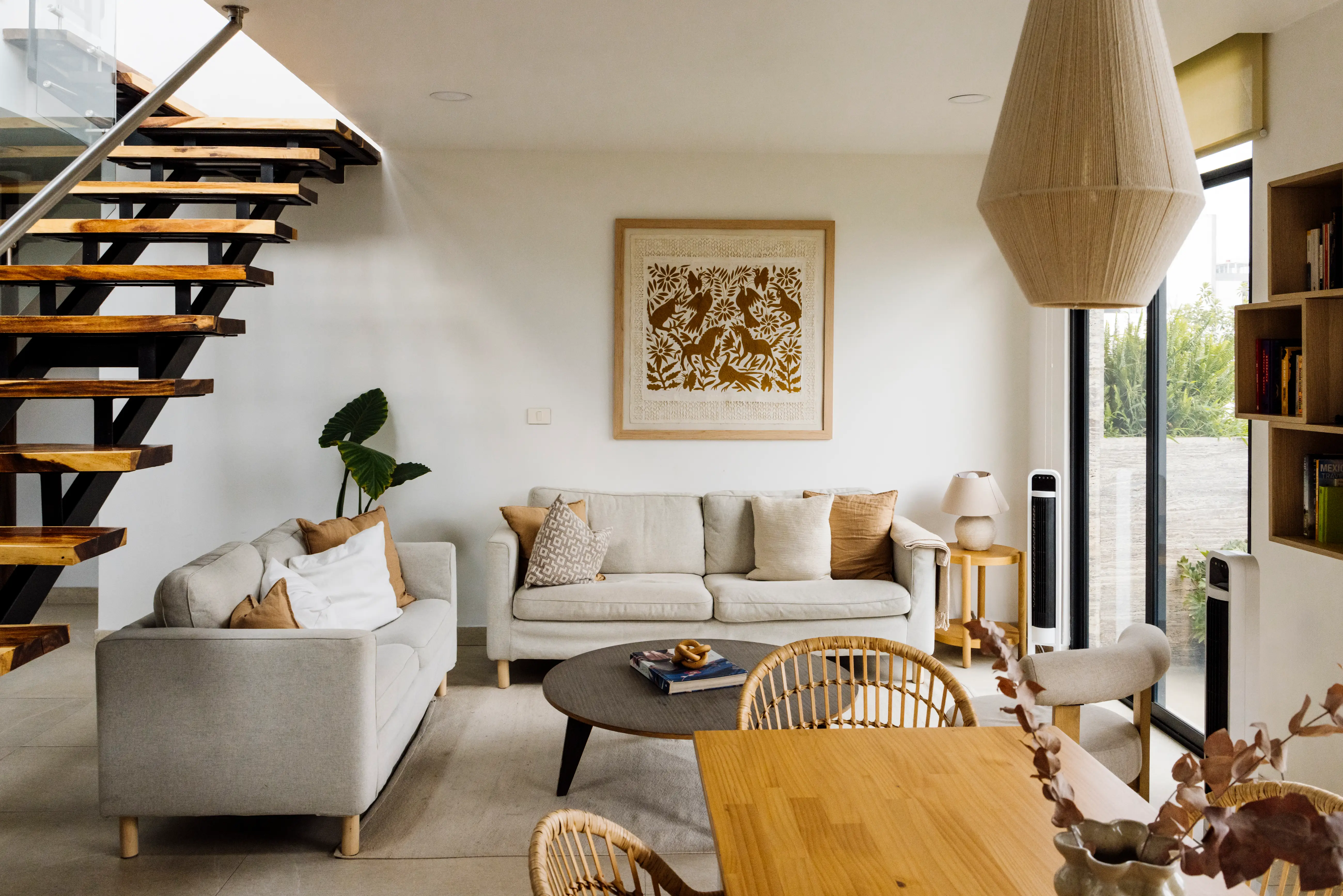 Living room with two couches, dining area, view of wooden stairs, artwork above couches