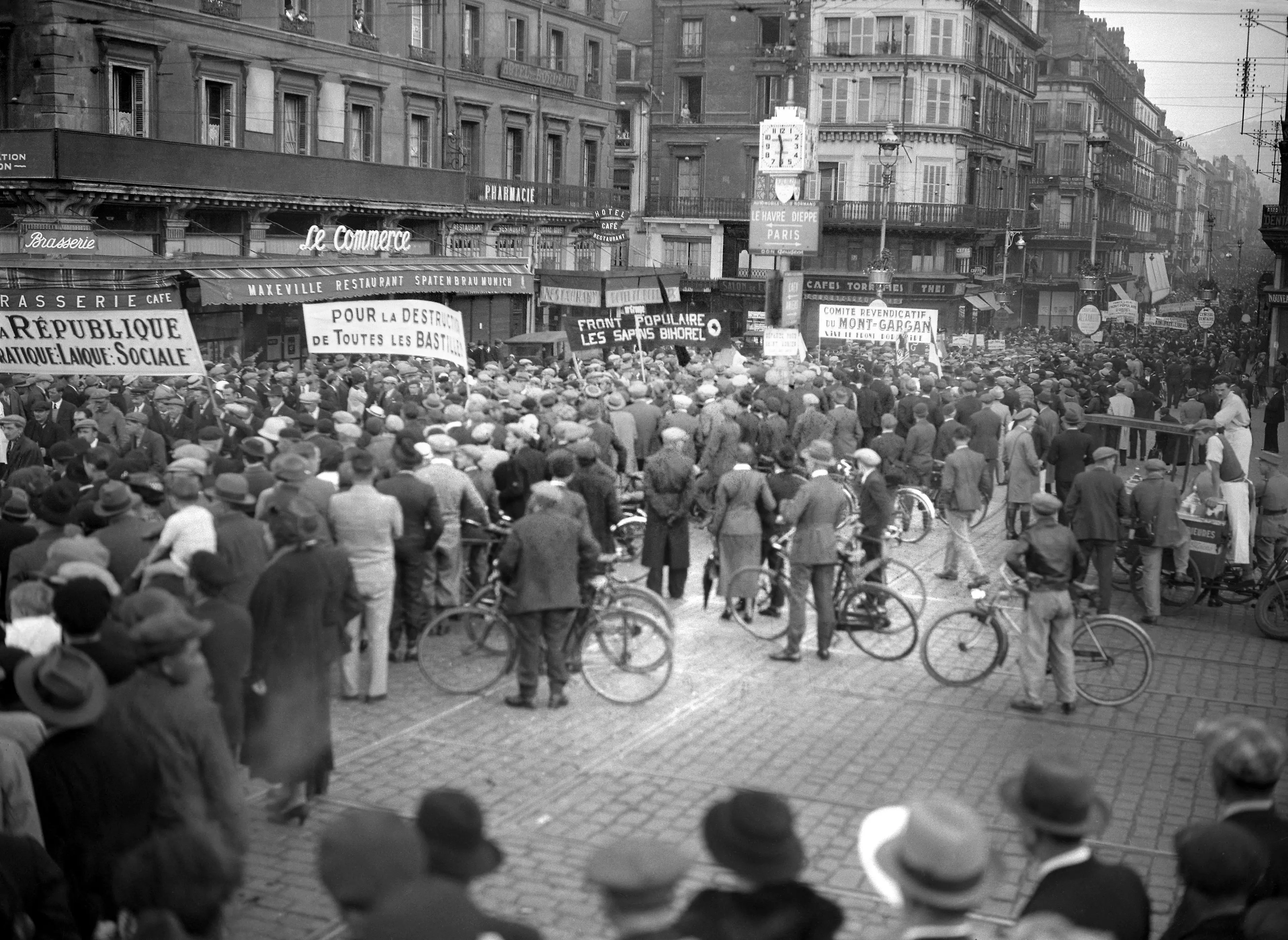 Crowd fills a city street during a black-and-white demonstration with banners, storefronts and bicycles.
