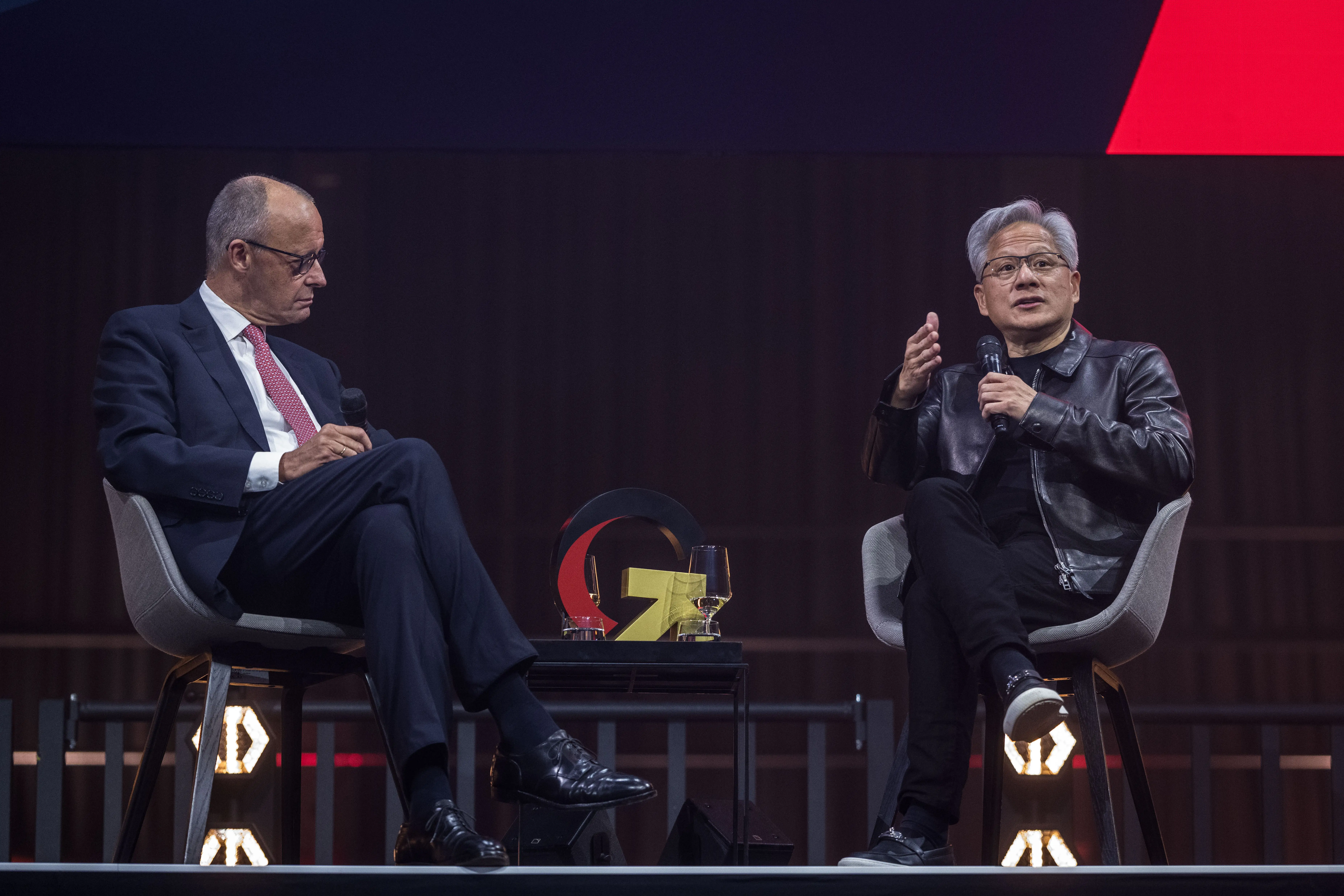 Jensen Huang speaks onstage beside another seated speaker during a conference discussion.