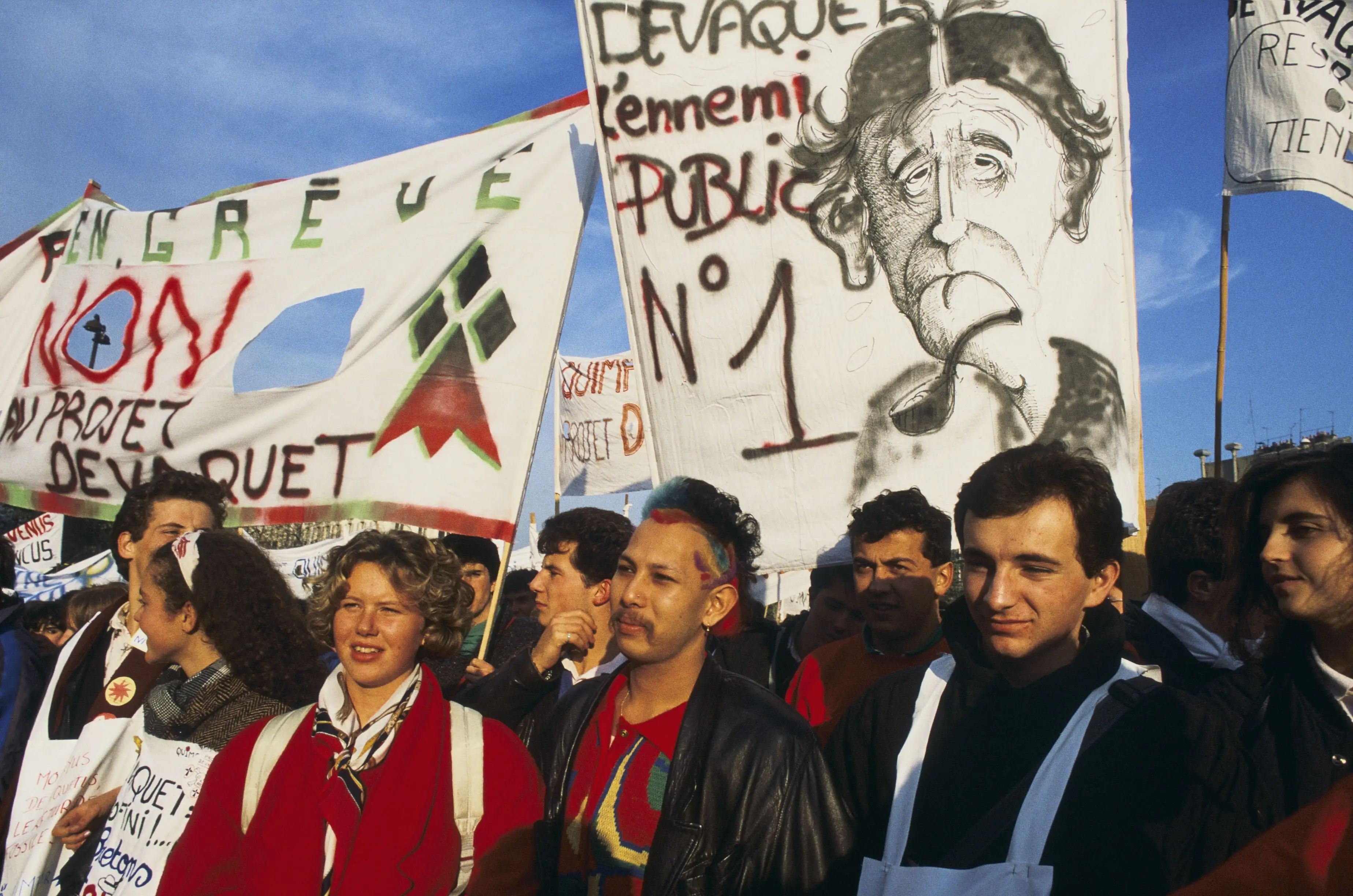 Demonstrators march with French protest banners reading “NON AU PROJET DEVAQUET” and “DEVAQUET l'ennemi PUBLIC N° 1.”