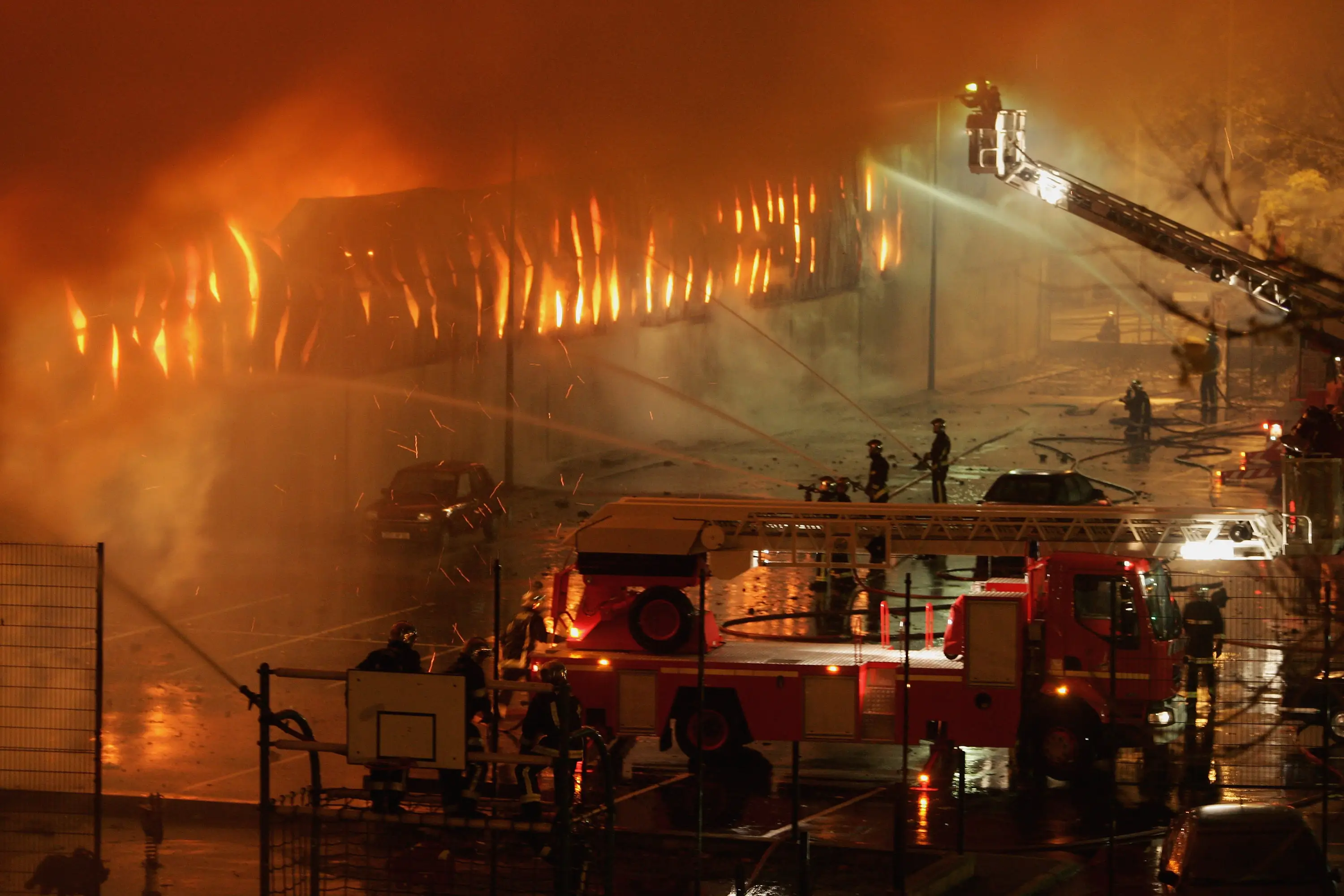 Firefighters use ladder trucks and hoses to battle a large building fire at night.