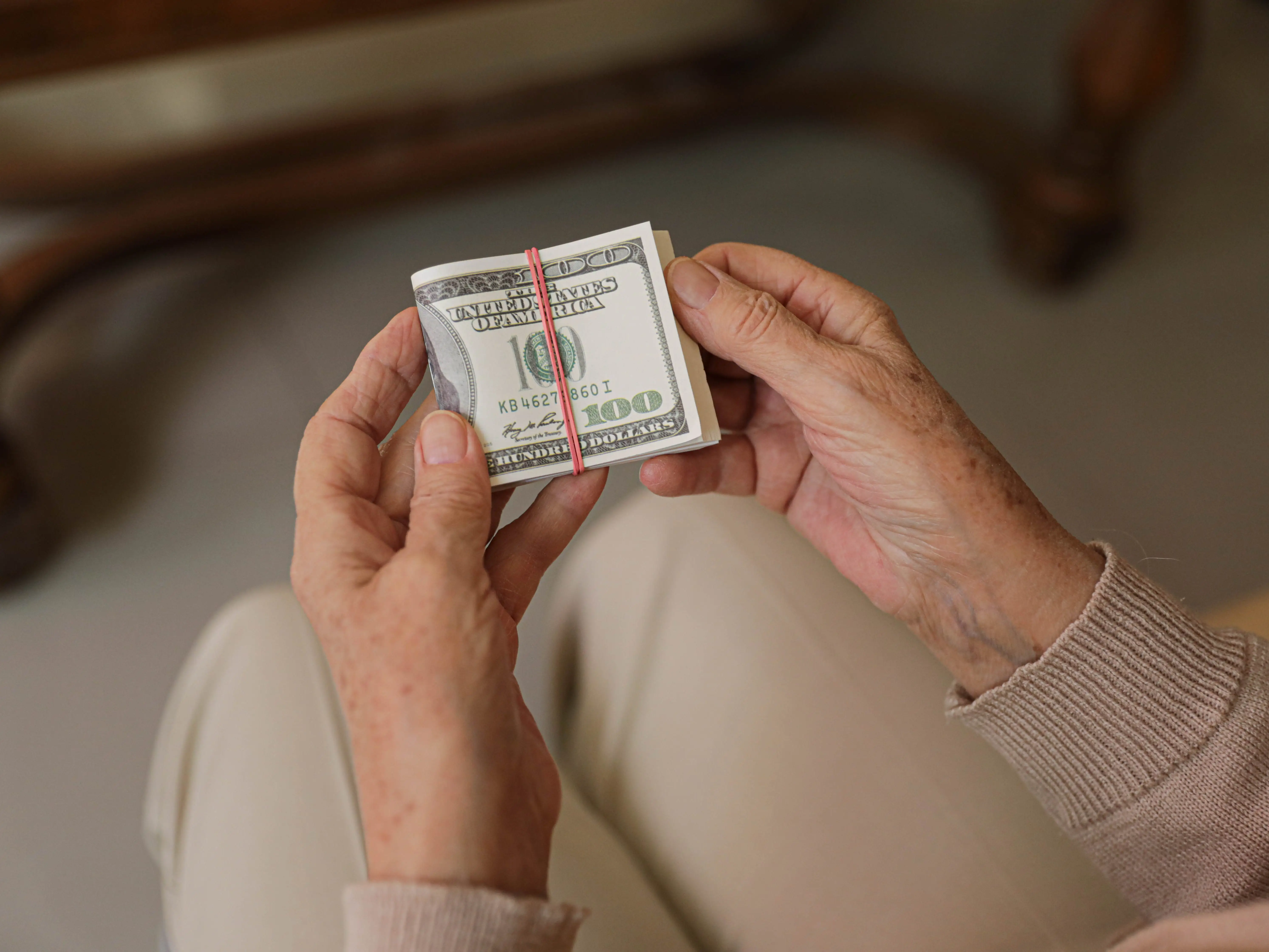 Hands holding a bundle of money, with a $100 bill visible, secured with a red band.