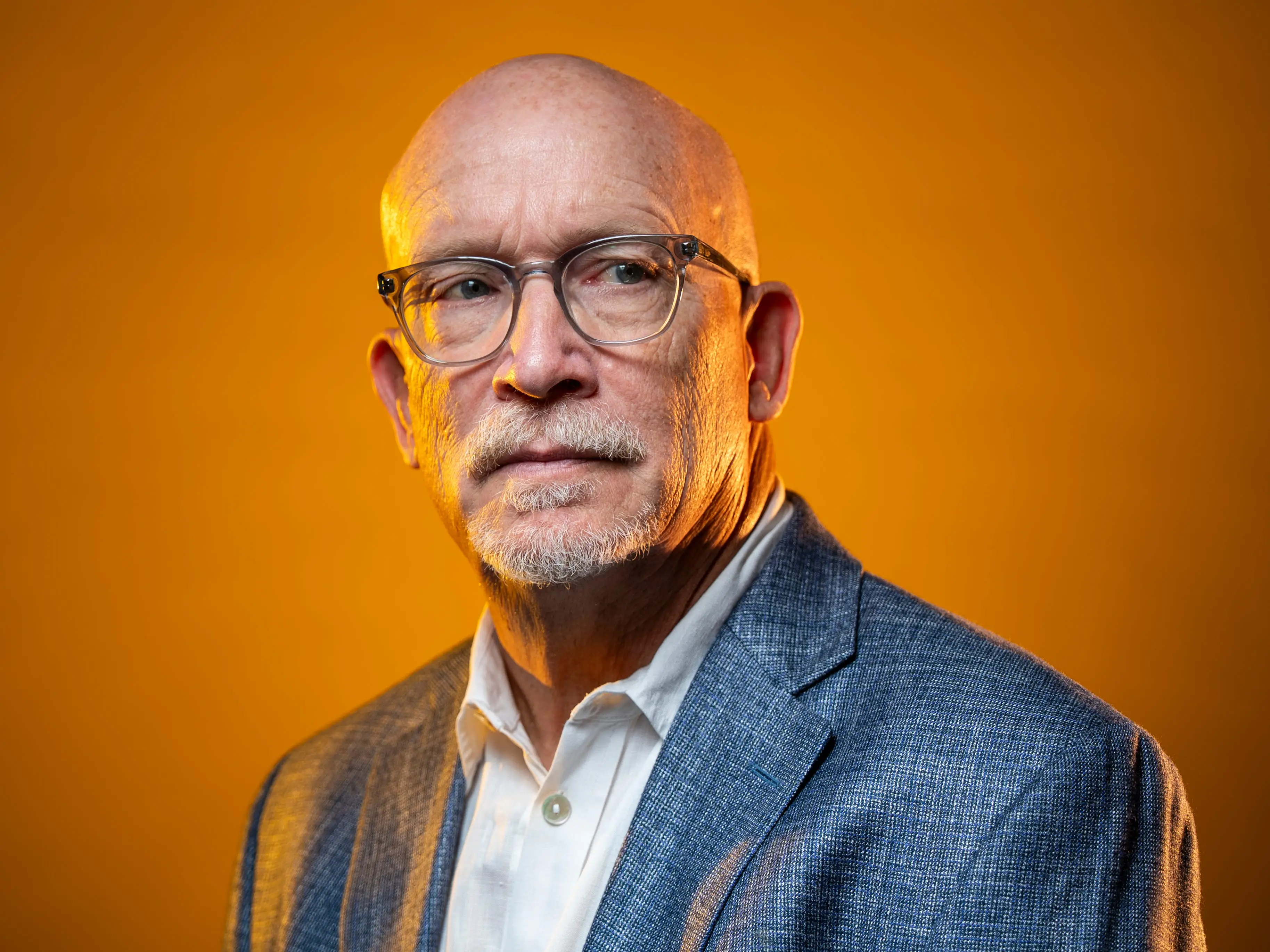 Alex Gibney sitting behind a yellow background