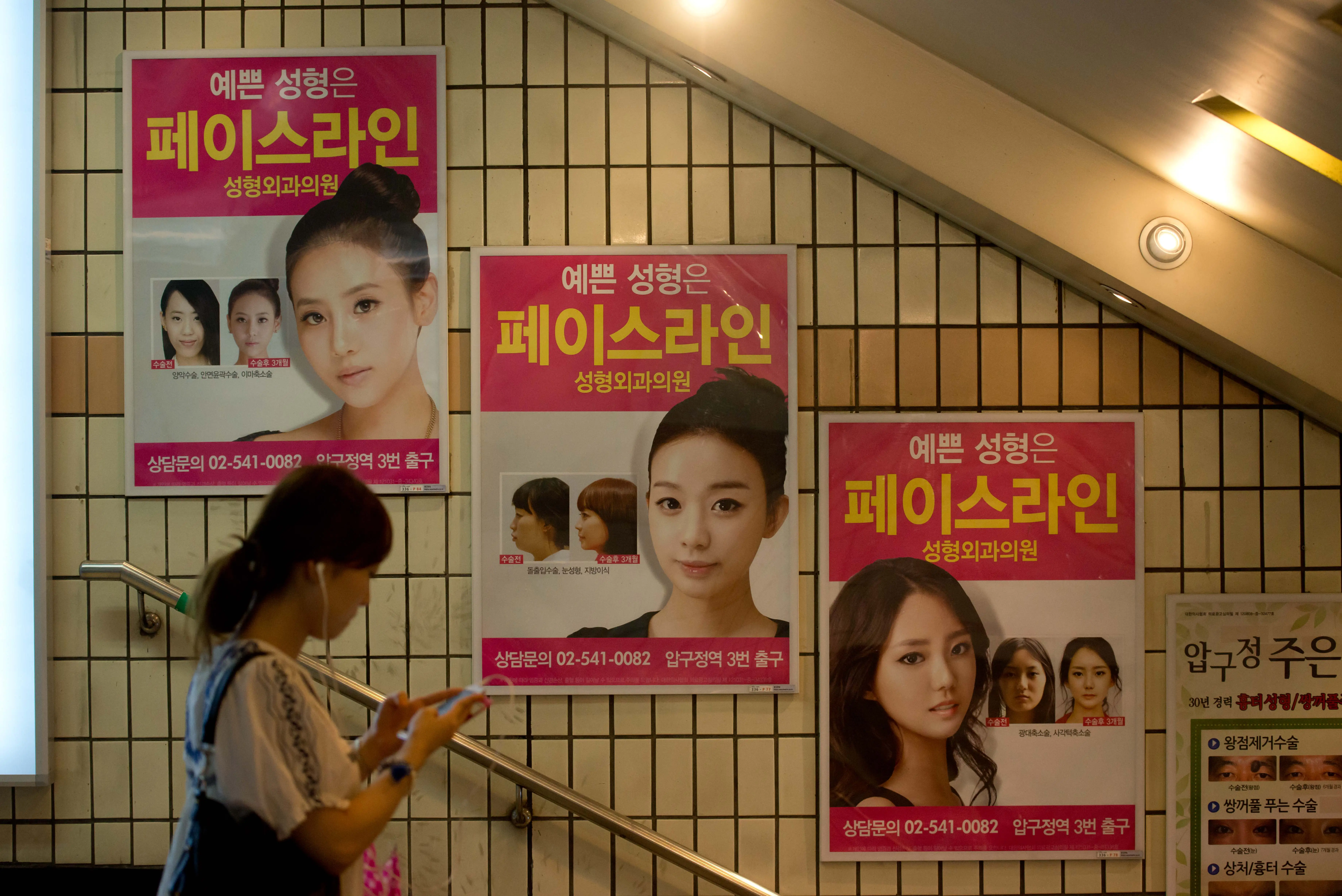 A person walks in a subway station by ads for plastic surgery.