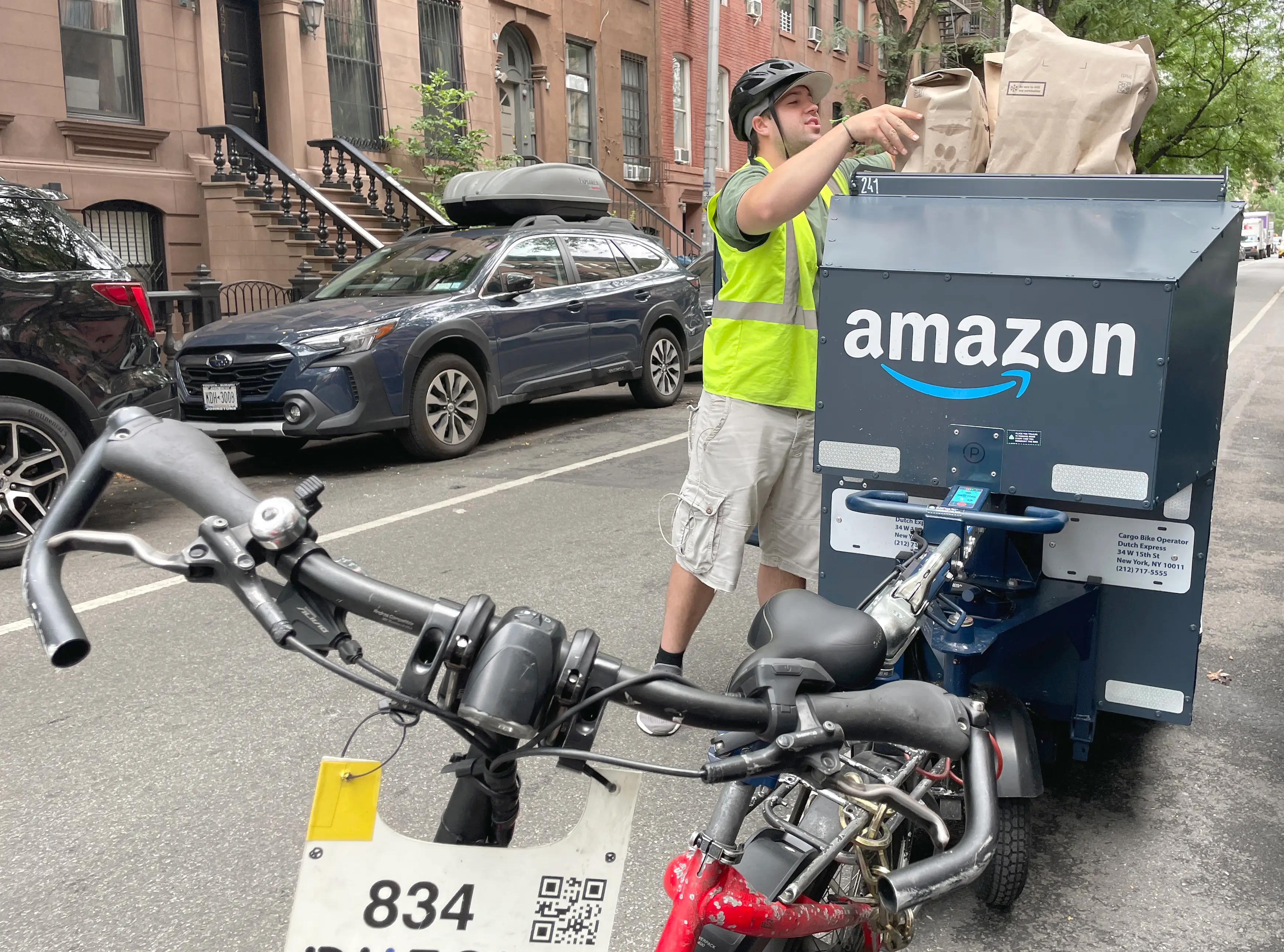 Amazon delivery worker loads paper bags into a cargo e-bike on a residential city street.