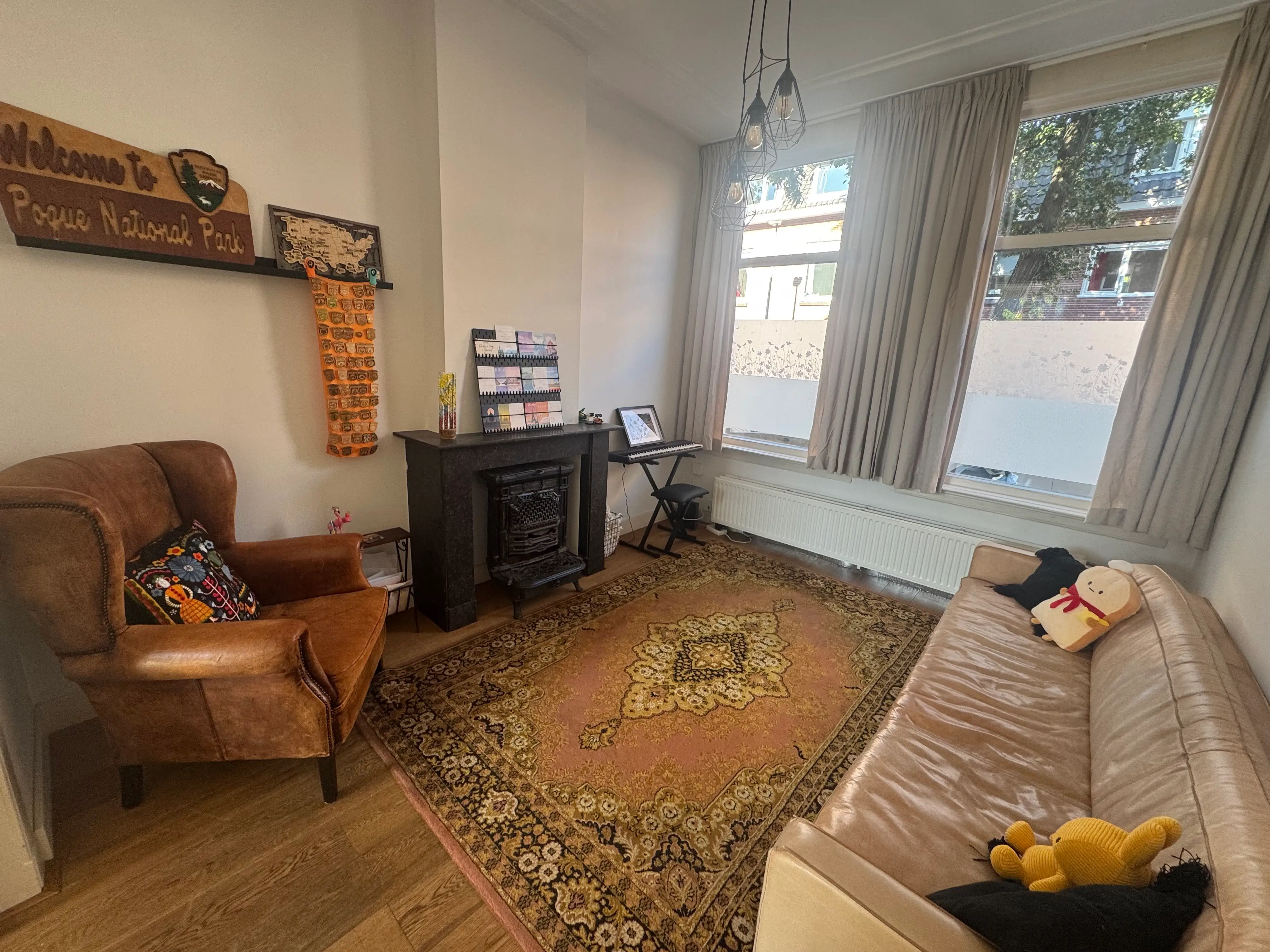 A living room with large windows, a couch, a chair, a fireplace, and a keyboard piano.