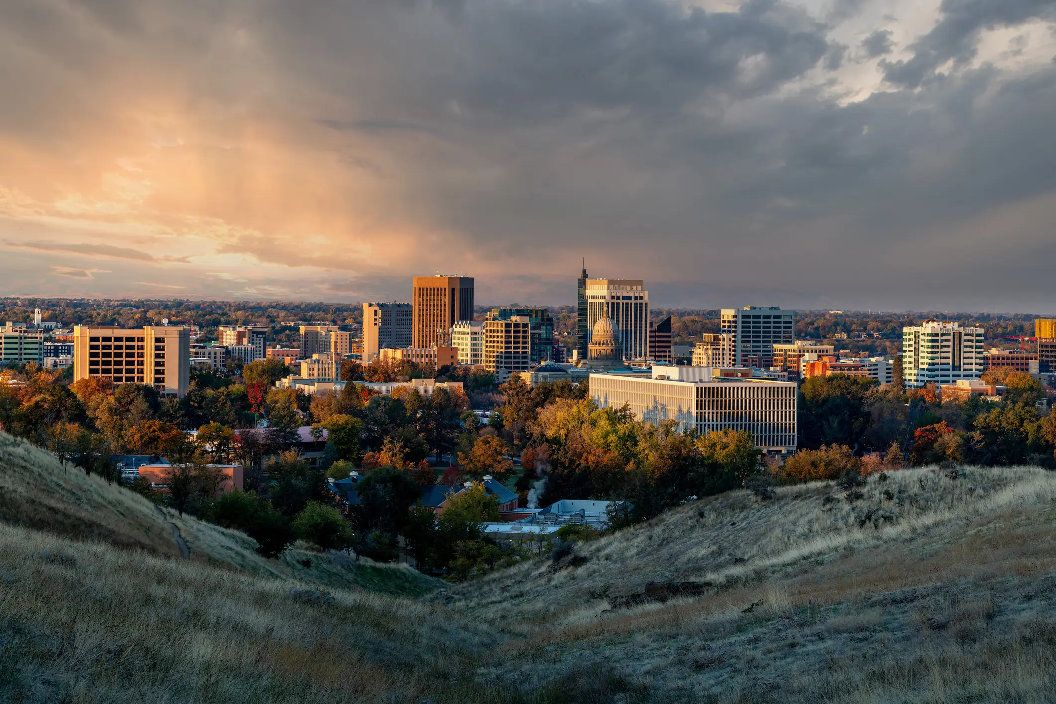 Downtown Boise skyline and the Idaho State Capitol are lit by sunset beneath dramatic storm clouds.