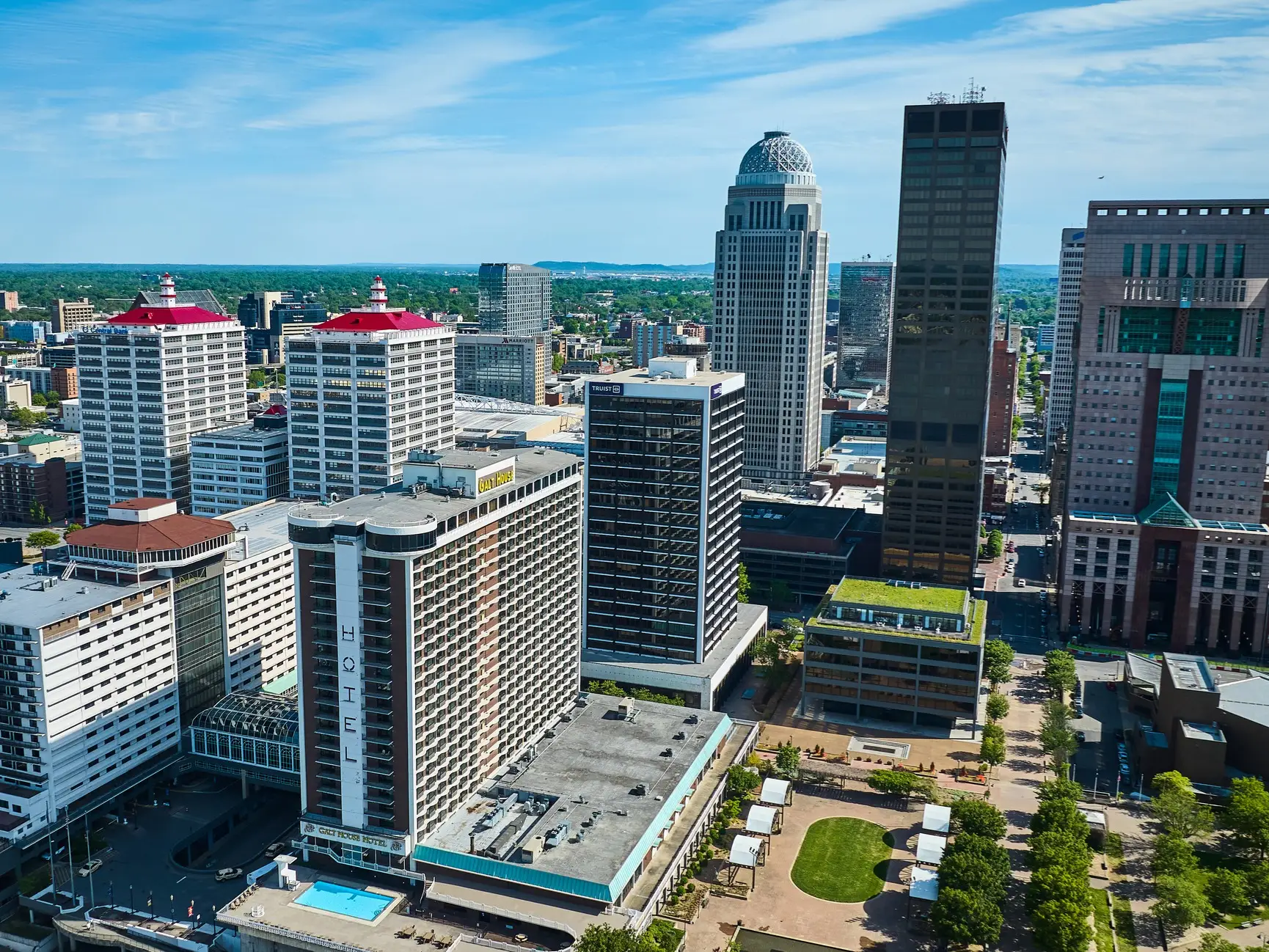 Aerial view of downtown Louisville skyscrapers and hotels, including the Galt House Hotel, under a clear blue sky.