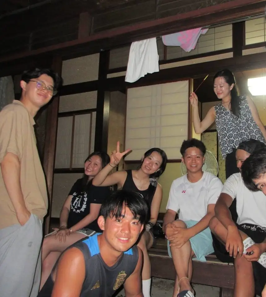 Group of smiling people posing in a wooden room with sliding panels and hanging laundry.