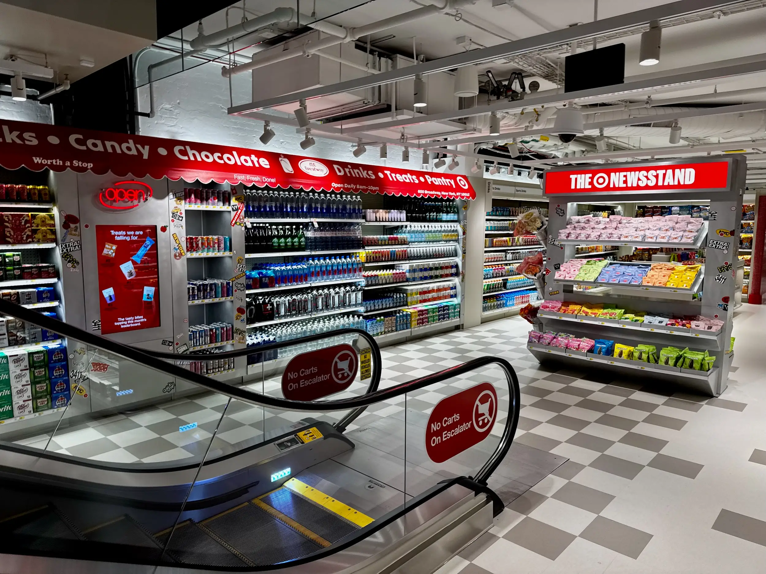 Convenience store candy and drink displays sit beside an escalator with THE ONEWSTAND sign.