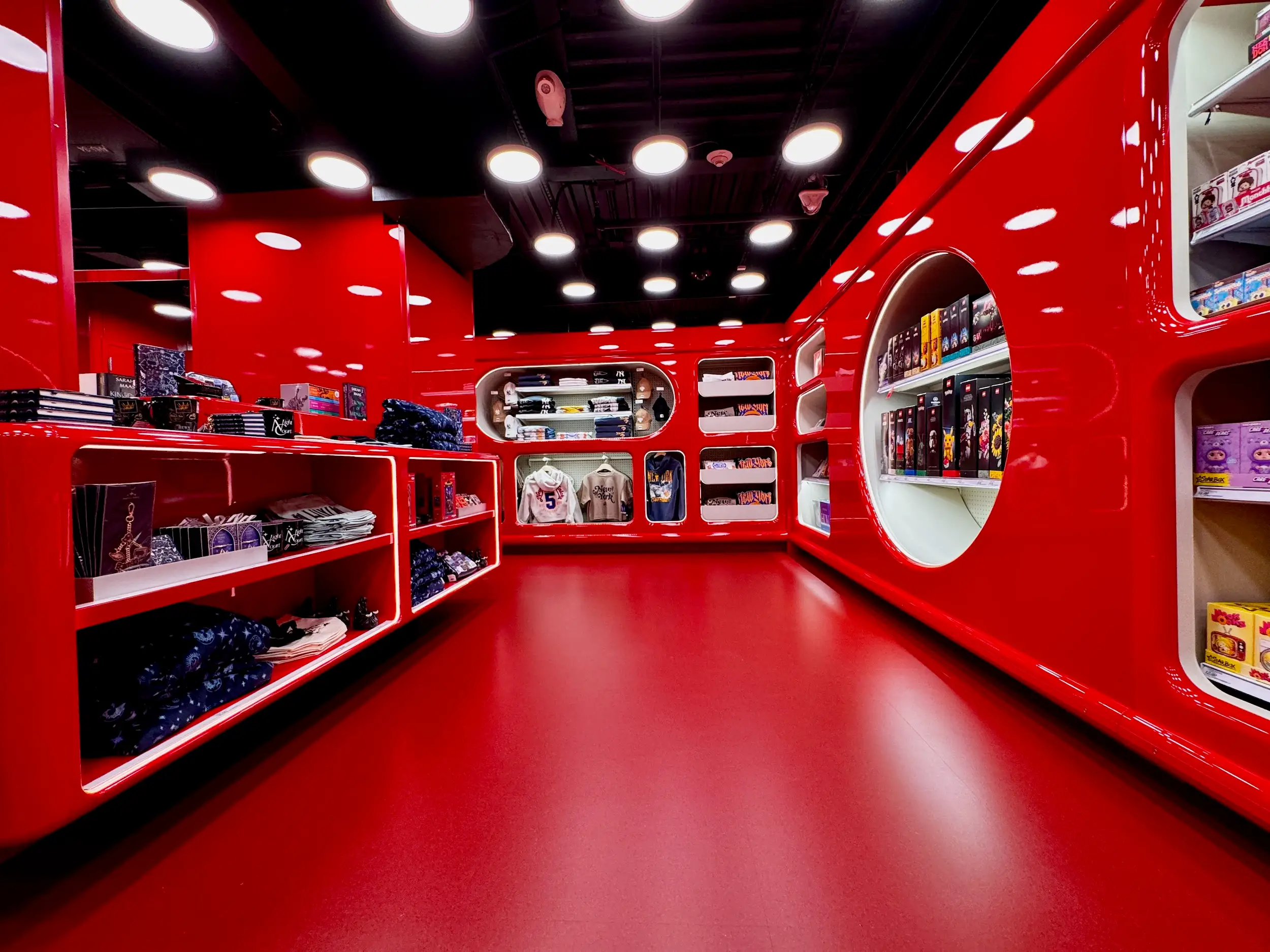 Bright red retail store interior with curved display shelves holding apparel, boxed collectibles, and sports jerseys.