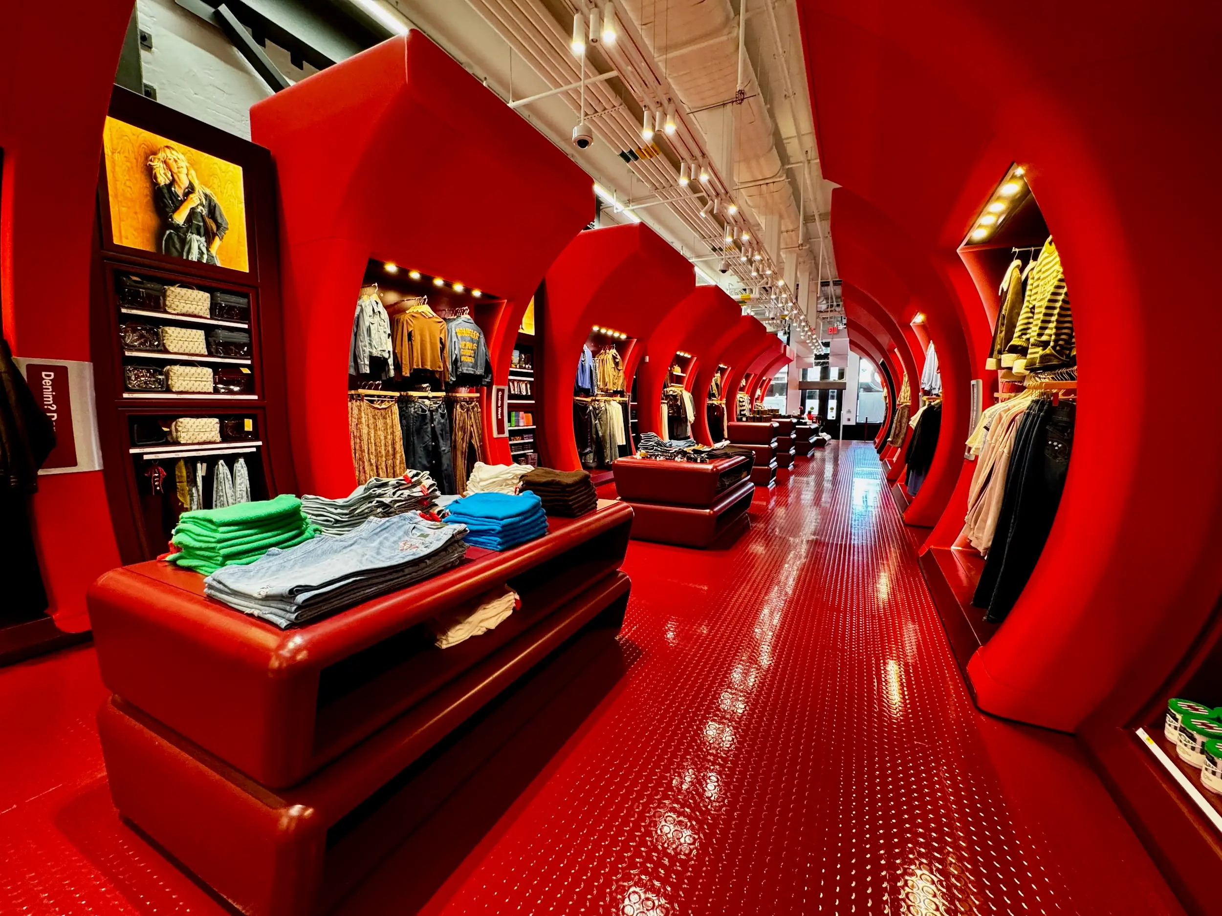 Bright red clothing store interior with circular arch displays, folded jeans, sweaters, and racks of apparel.