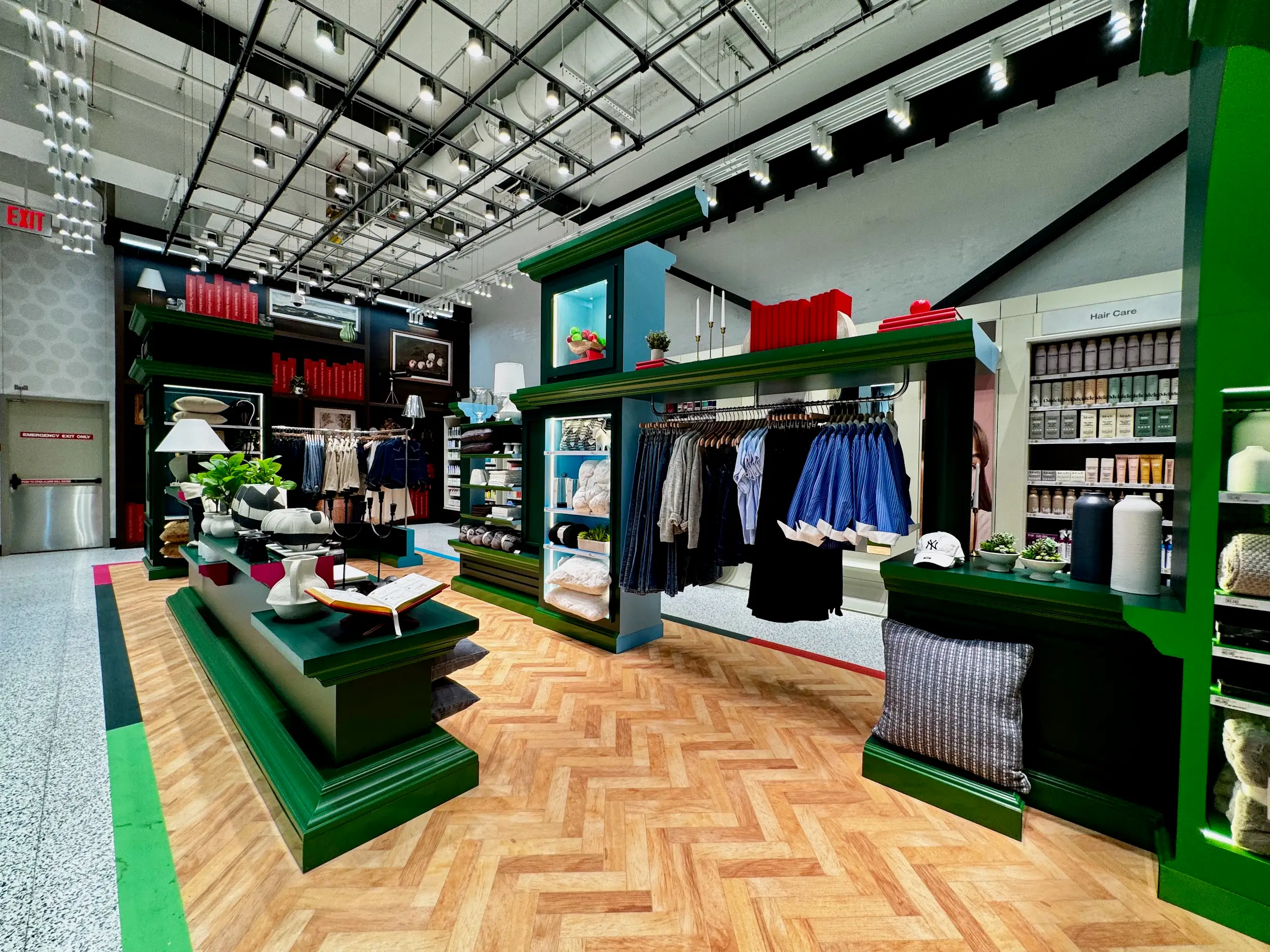 Colorful retail store interior with clothing racks, home goods displays, hair care shelves, and green built-in fixtures.