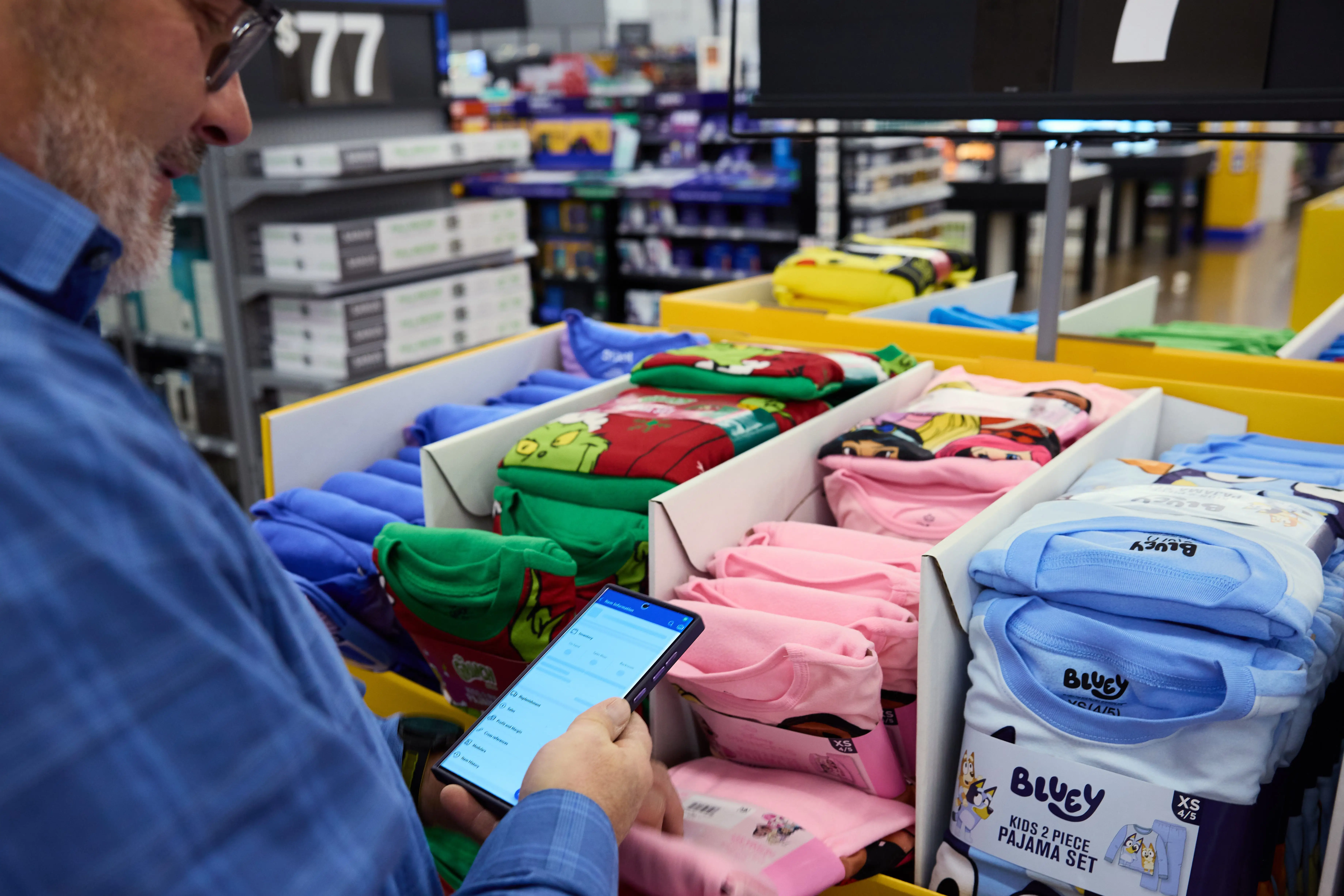 A person uses a smartphone beside a retail display of folded Bluey children's pajama sets.