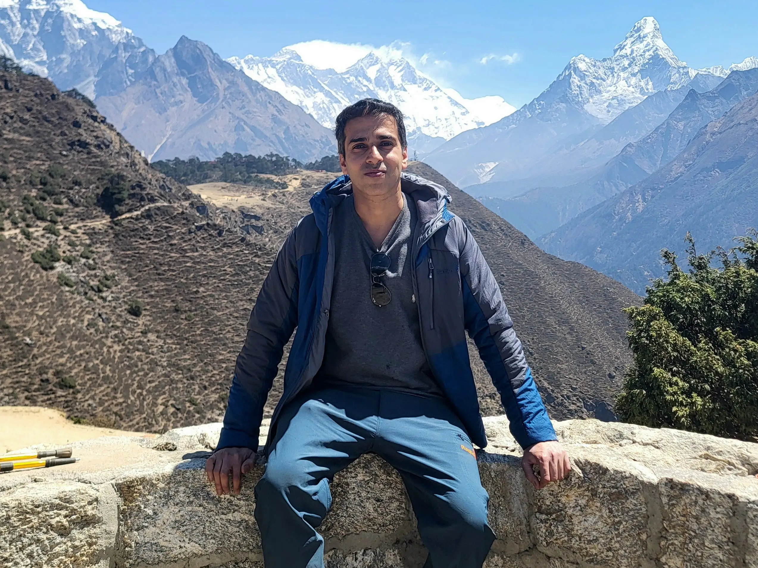 Mihirkant Upadhyaya is sitting on a wall in front of snowy mountains.