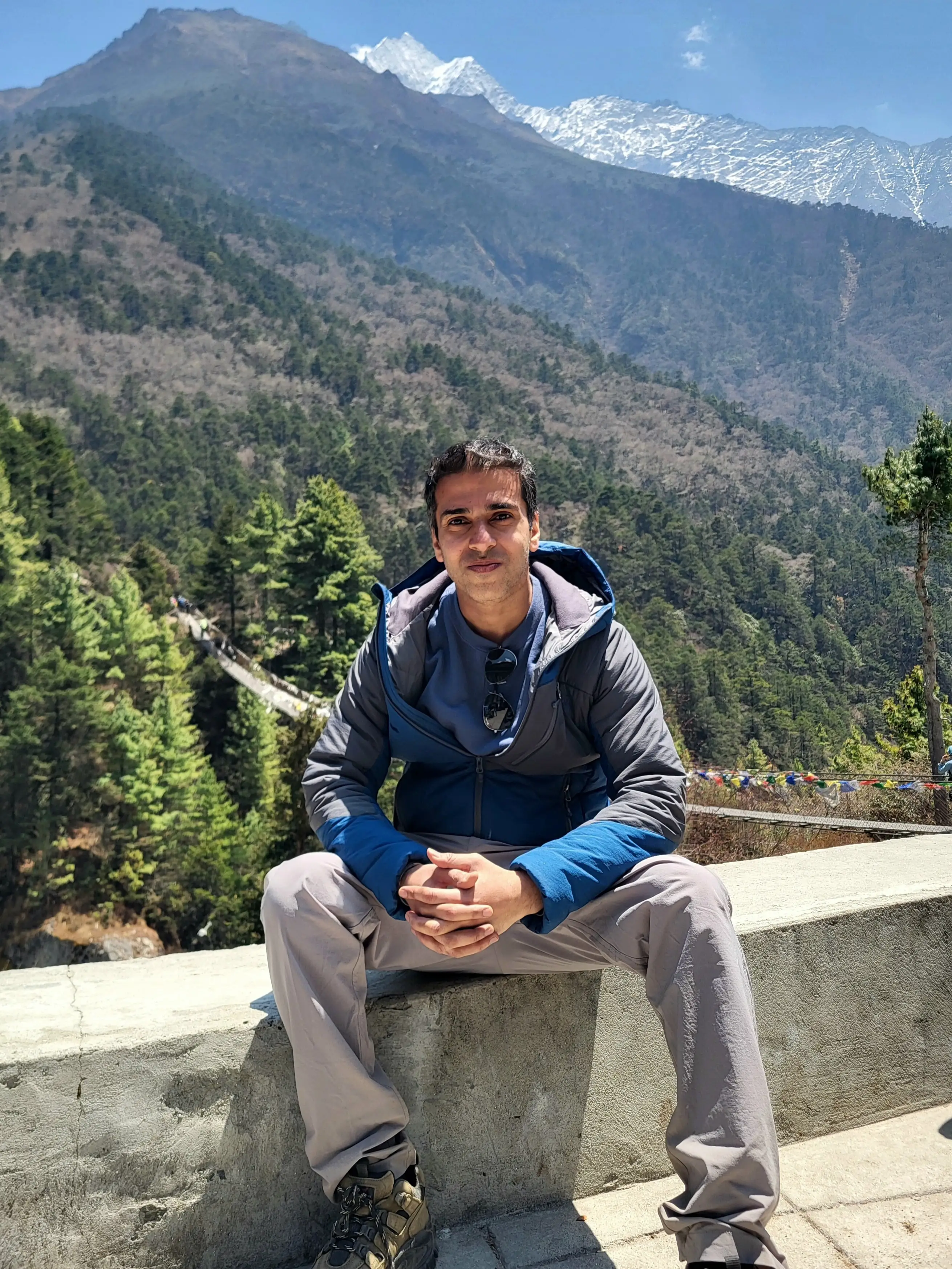 Upadhyaya is sitting on a wall in front of a mountain and trees.