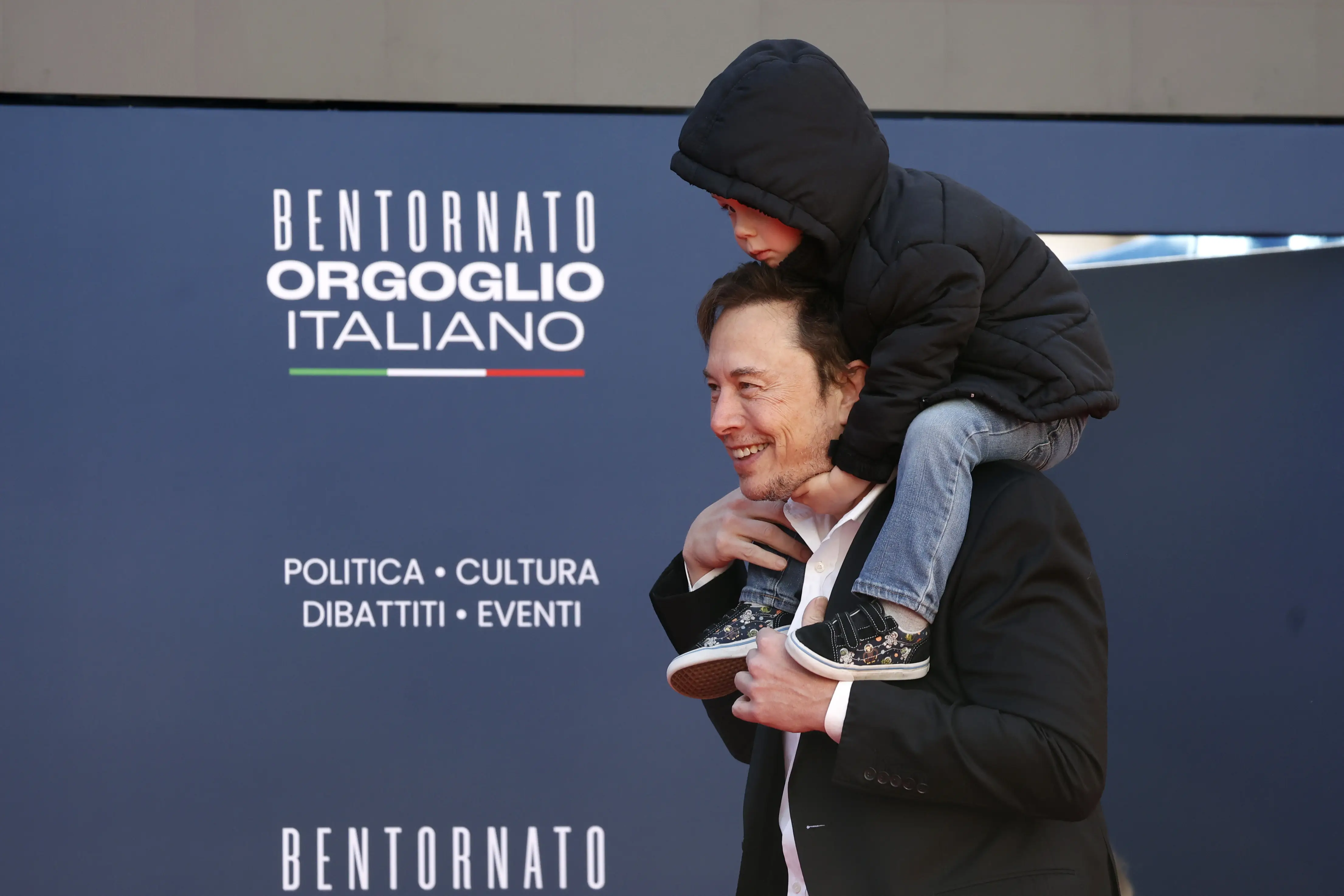 Elon Musk holds one of his children on his shoulders.