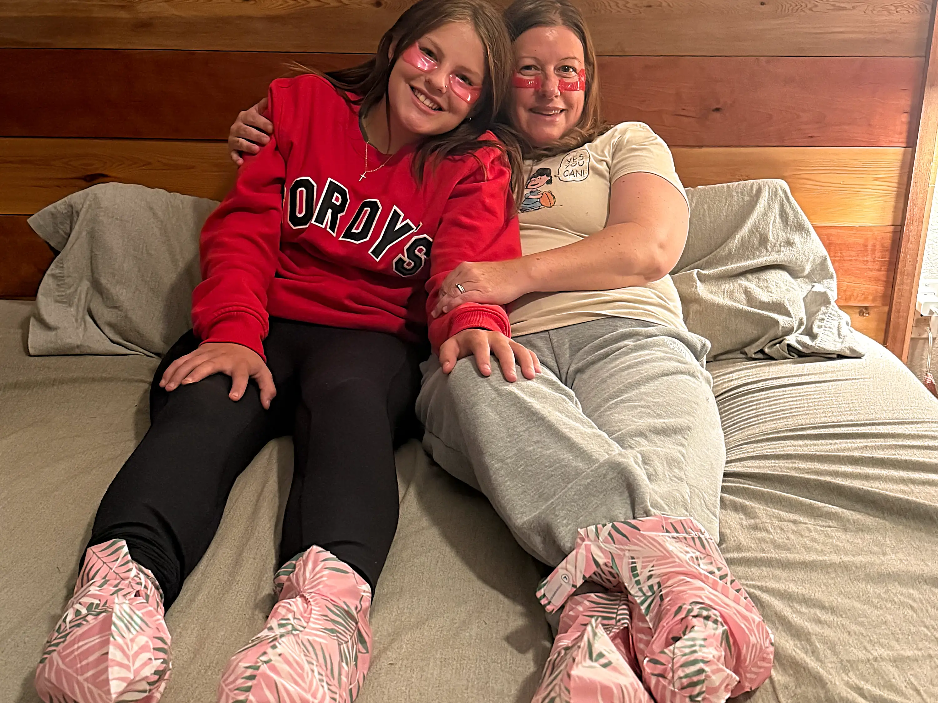 Two smiling people with pink face paint sit together on a bed in matching patterned slippers.
