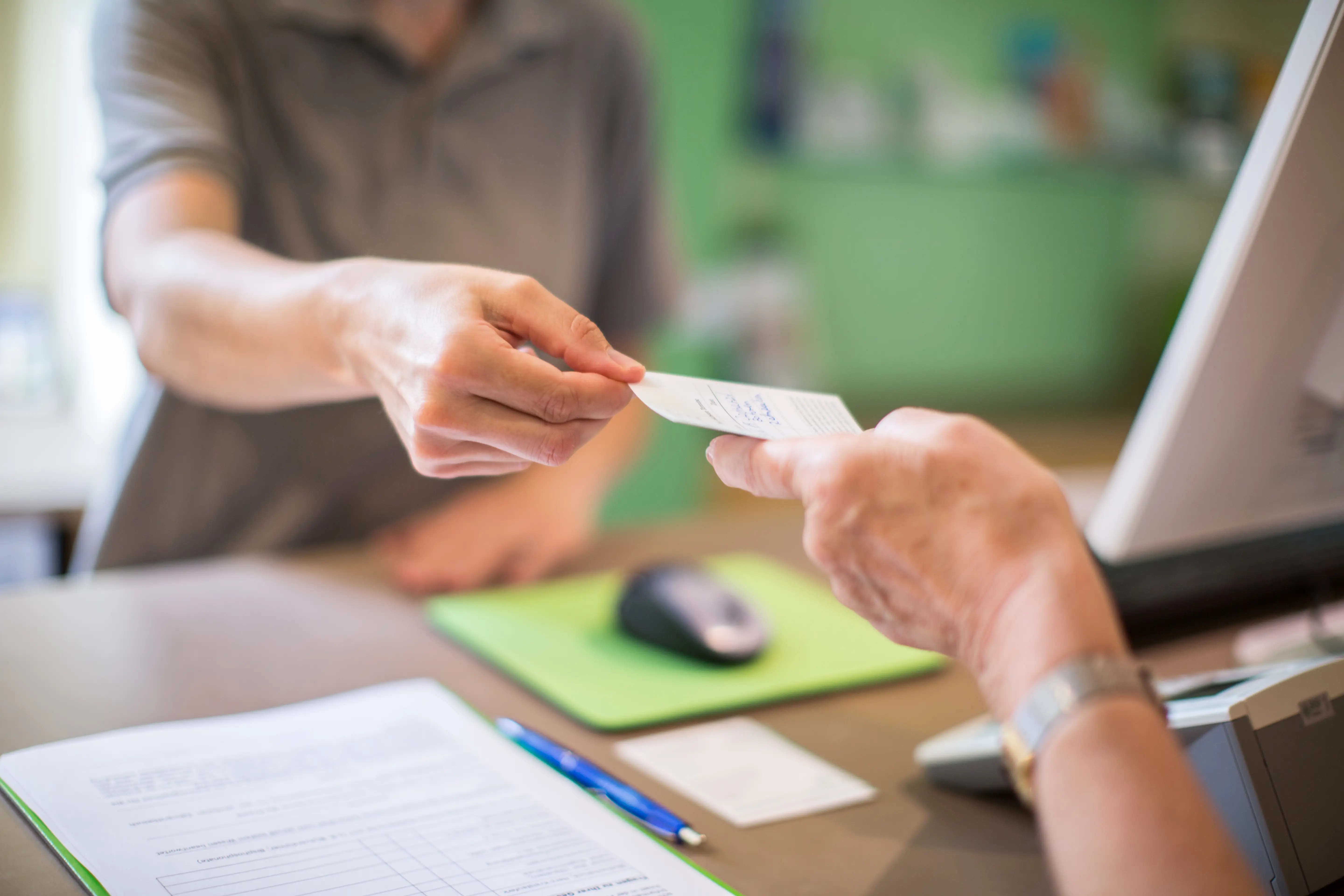 Close-up of a receptionist giving a health card to female patient at clinic. Focus on hands of female with a health card.