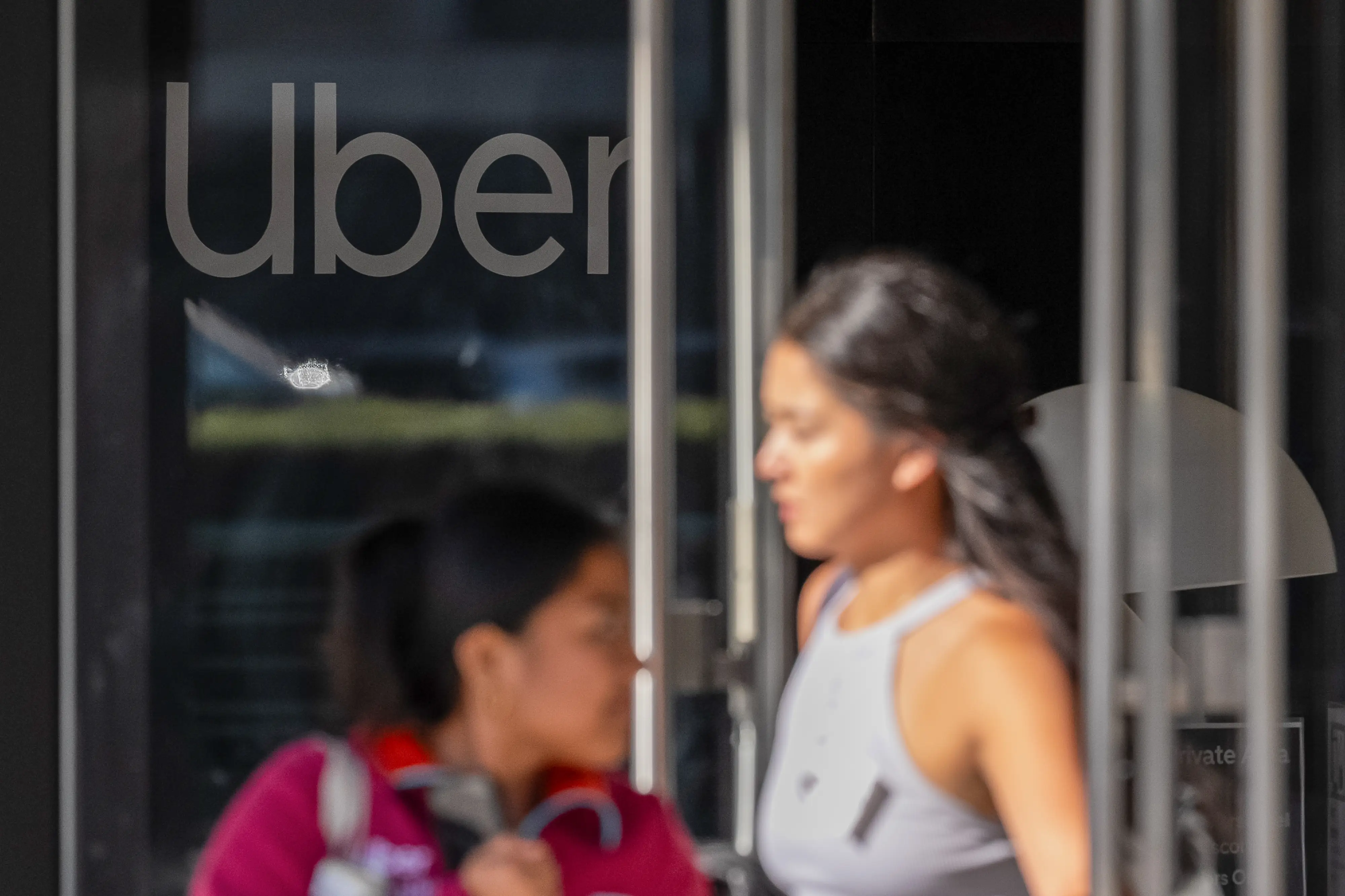 Blurred pedestrians pass an entrance with a large Uber logo on the glass door.