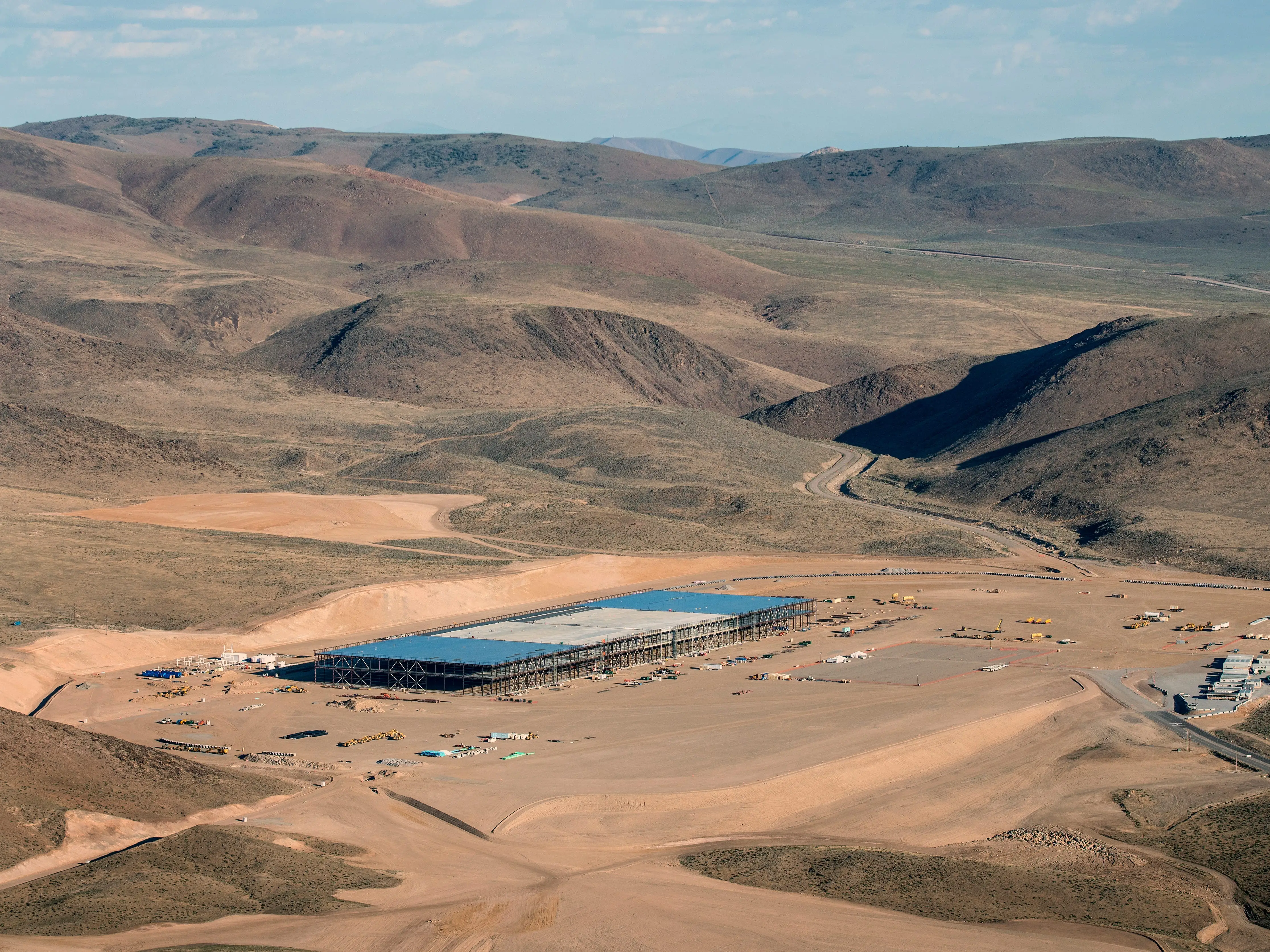 Aerial view of a large construction site with a partially built structure in a dry hilly desert landscape.