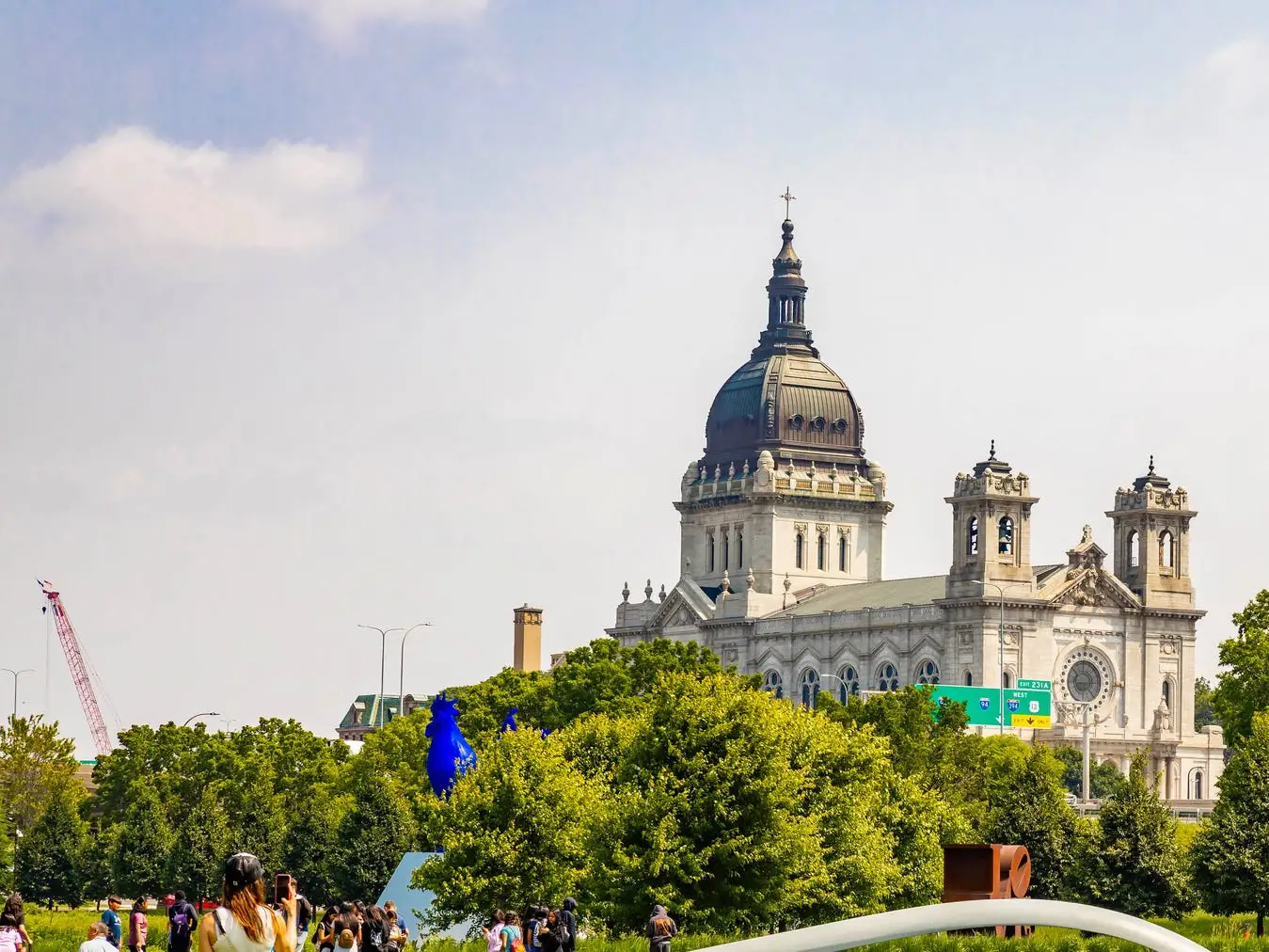 Spoonbridge and Cherry sculpture spans a pond in a green park with the Basilica of Saint Mary in the background.