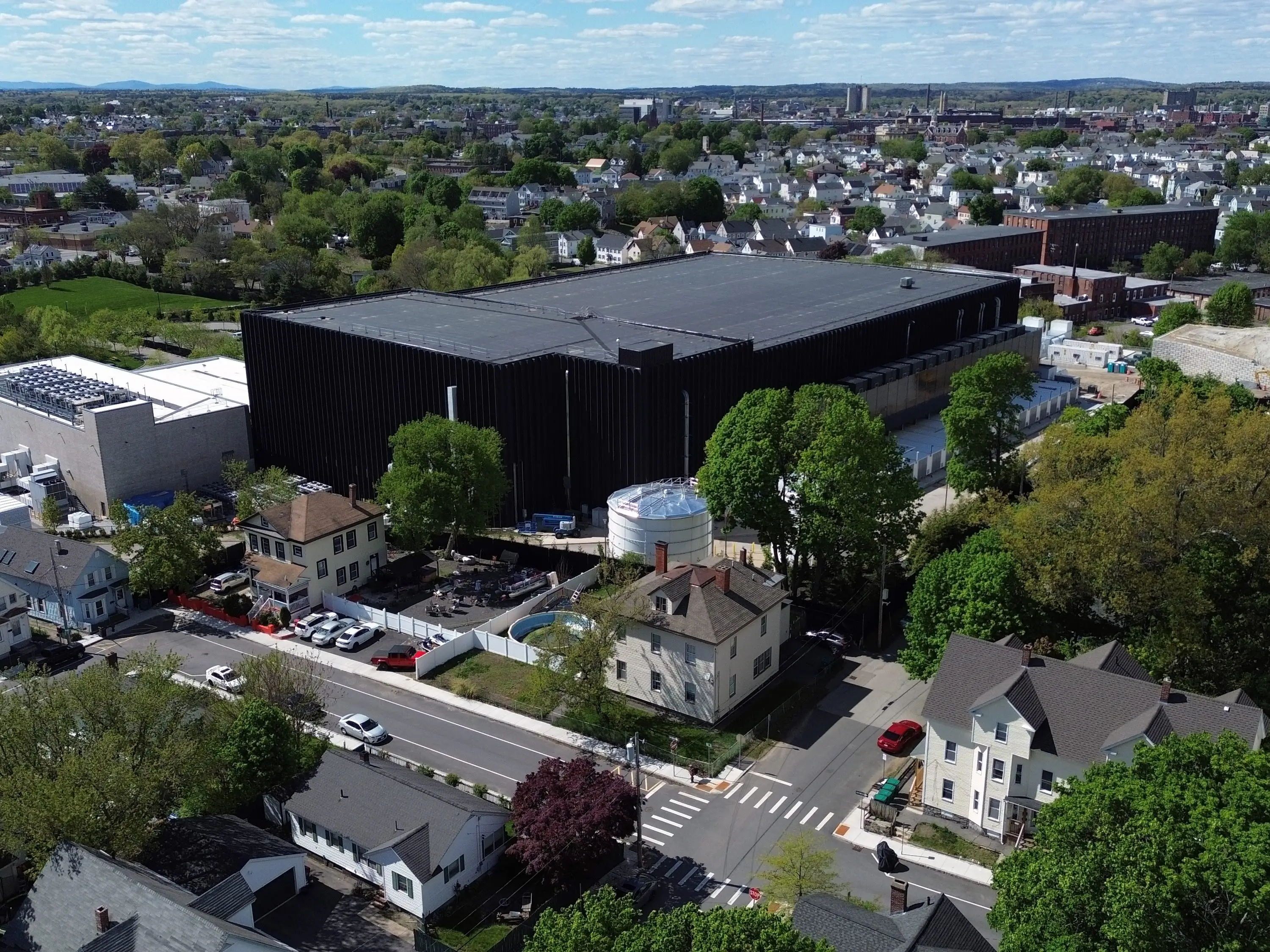 Aerial view of a neighborhood with houses, tree-lined streets, and a large black industrial building.