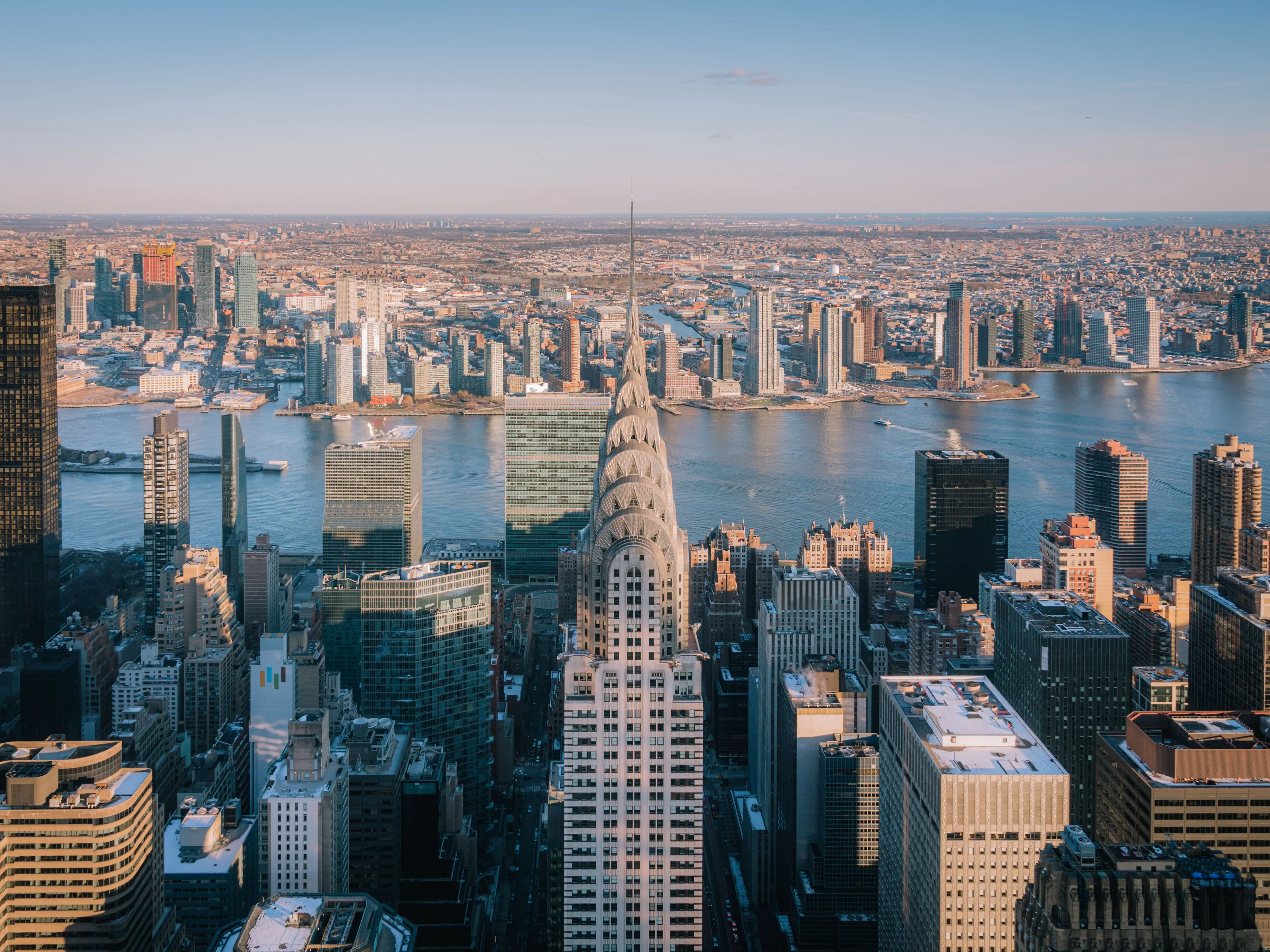Aerial view of New York City skyline featuring the Chrysler Building and East River under a clear blue sky.
