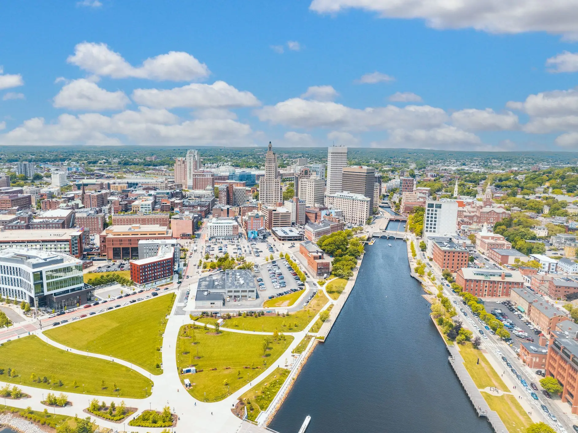 Aerial view of downtown Providence skyline beside the Providence River under a partly cloudy blue sky.