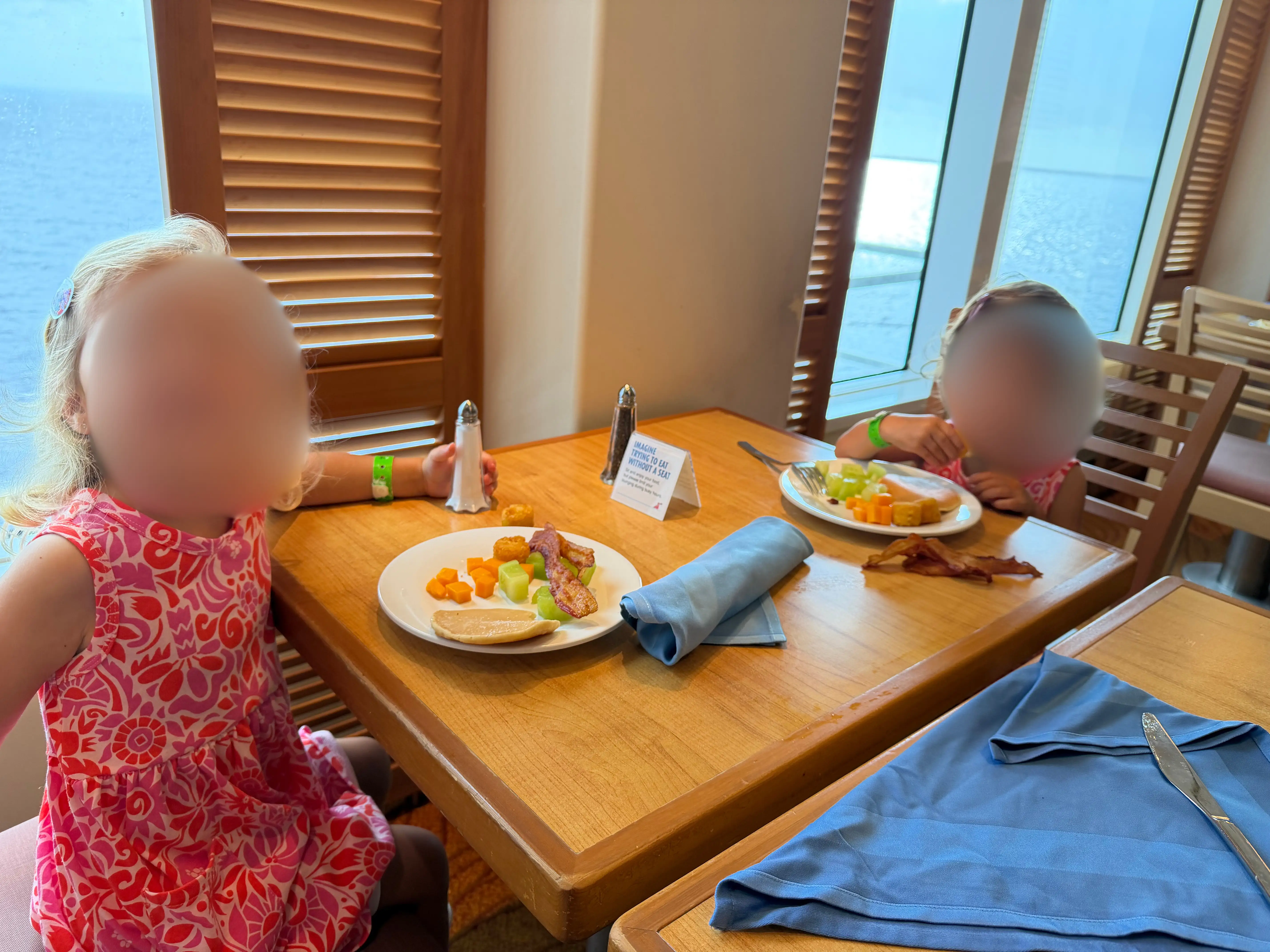 Two kids with blurred faces at table eating breakfast