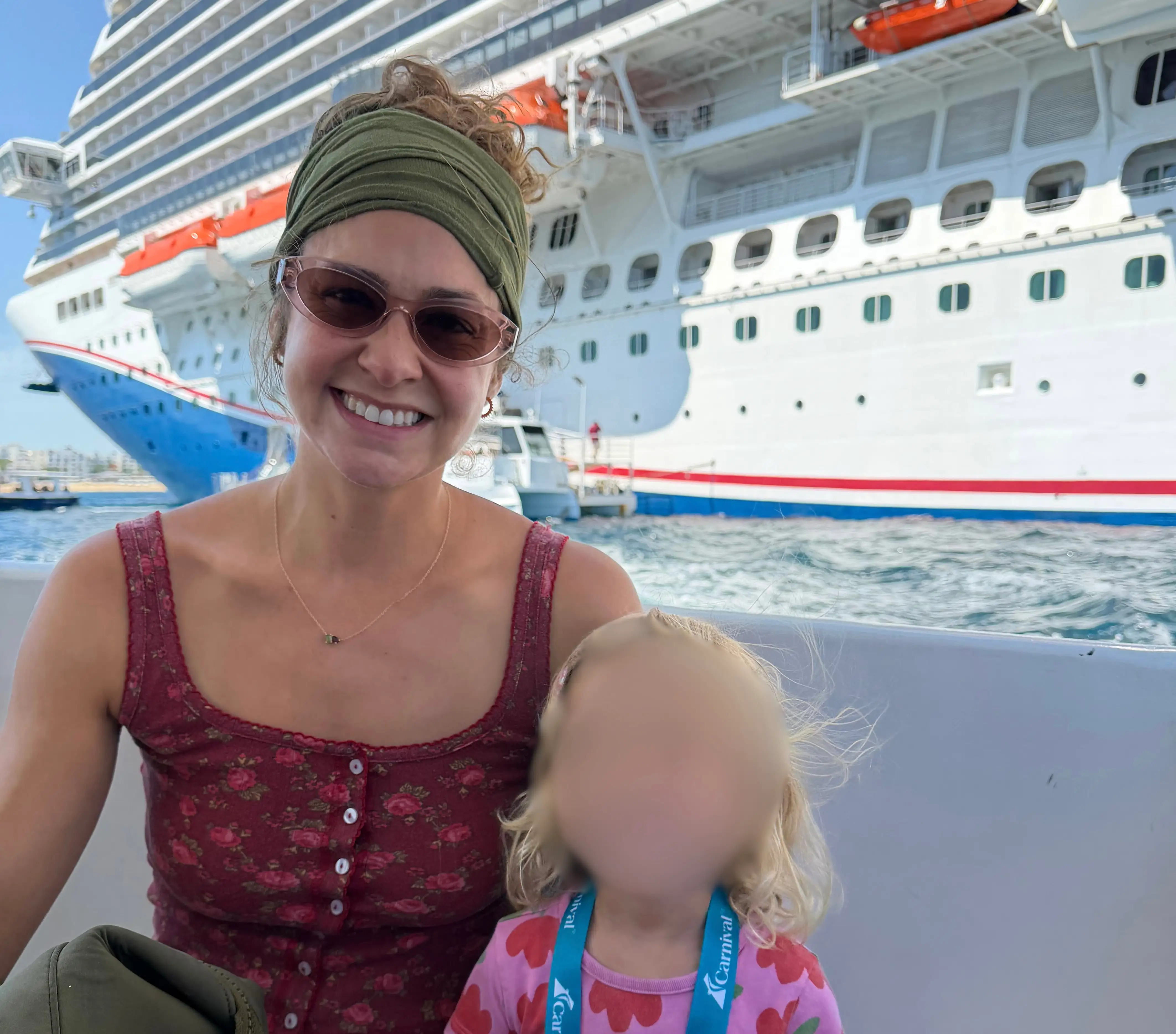 Woman smiling next to kid with blurred face, cruise ship in background