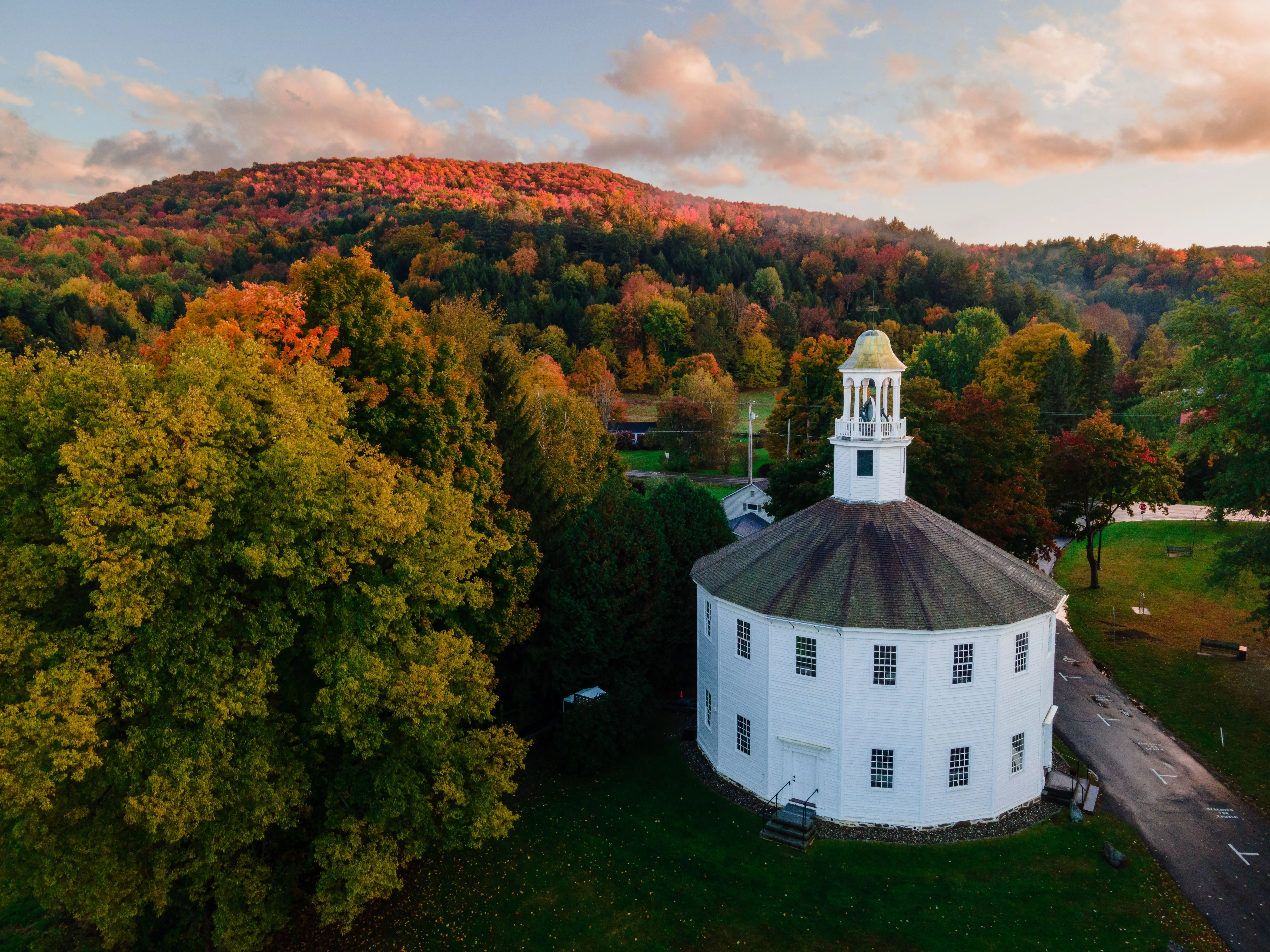 An aerial view of the old round church in Richmond, Vermont, surrounded by a breathtaking view of a green forest at sunset