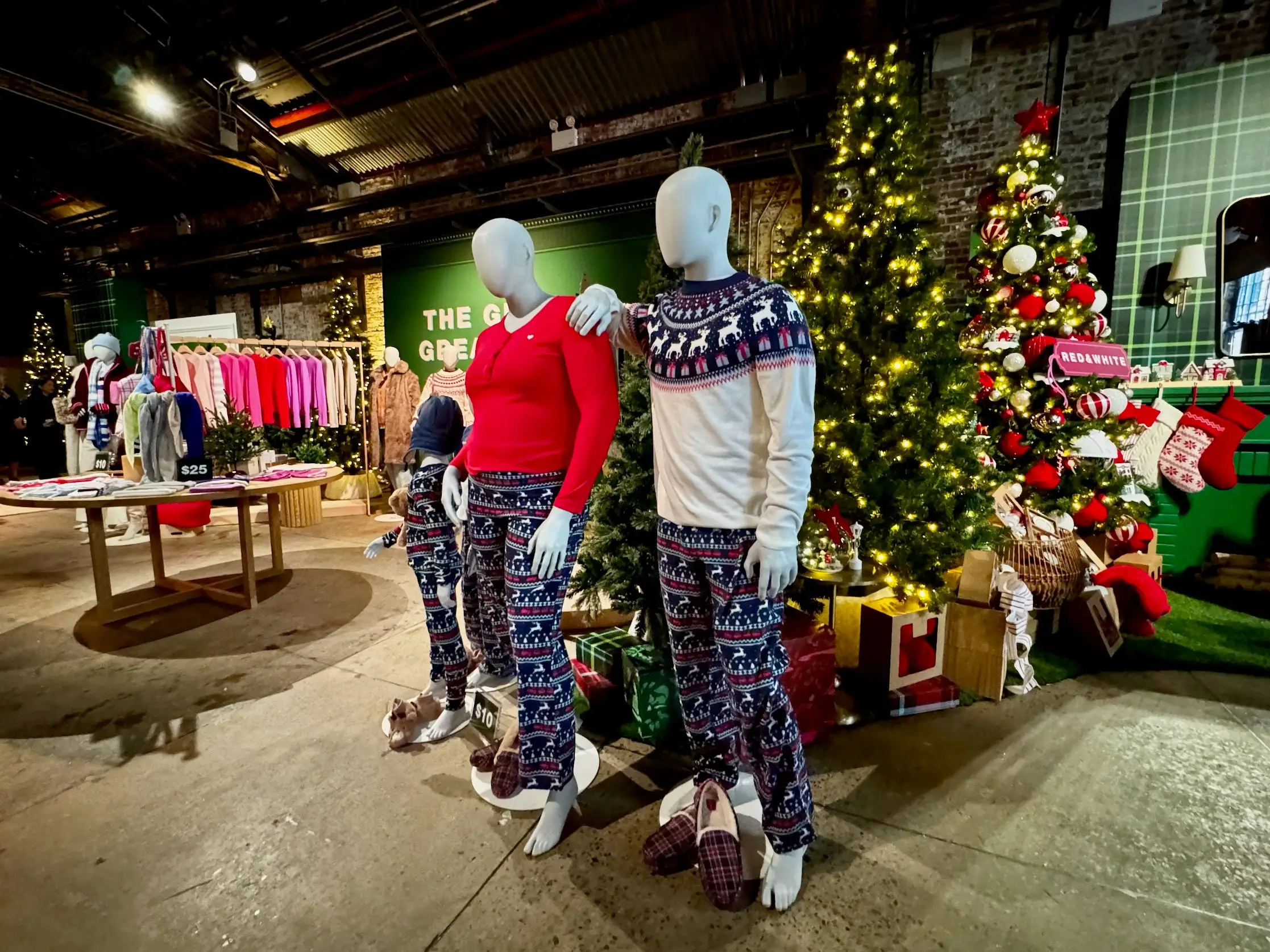 Mannequins in matching holiday pajamas stand beside decorated Christmas trees in a festive retail display.