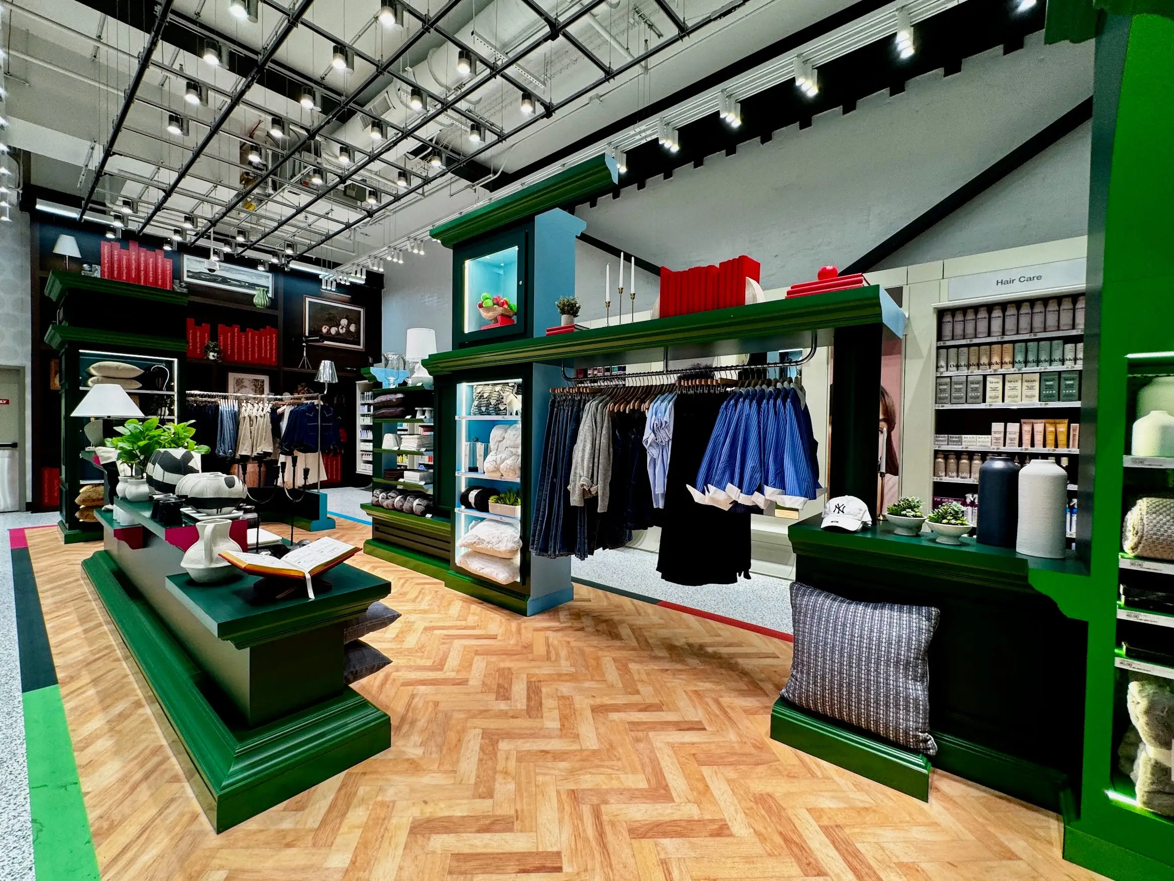 Colorful retail store interior with clothing racks, home goods displays, hair care shelves, and green built-in fixtures.