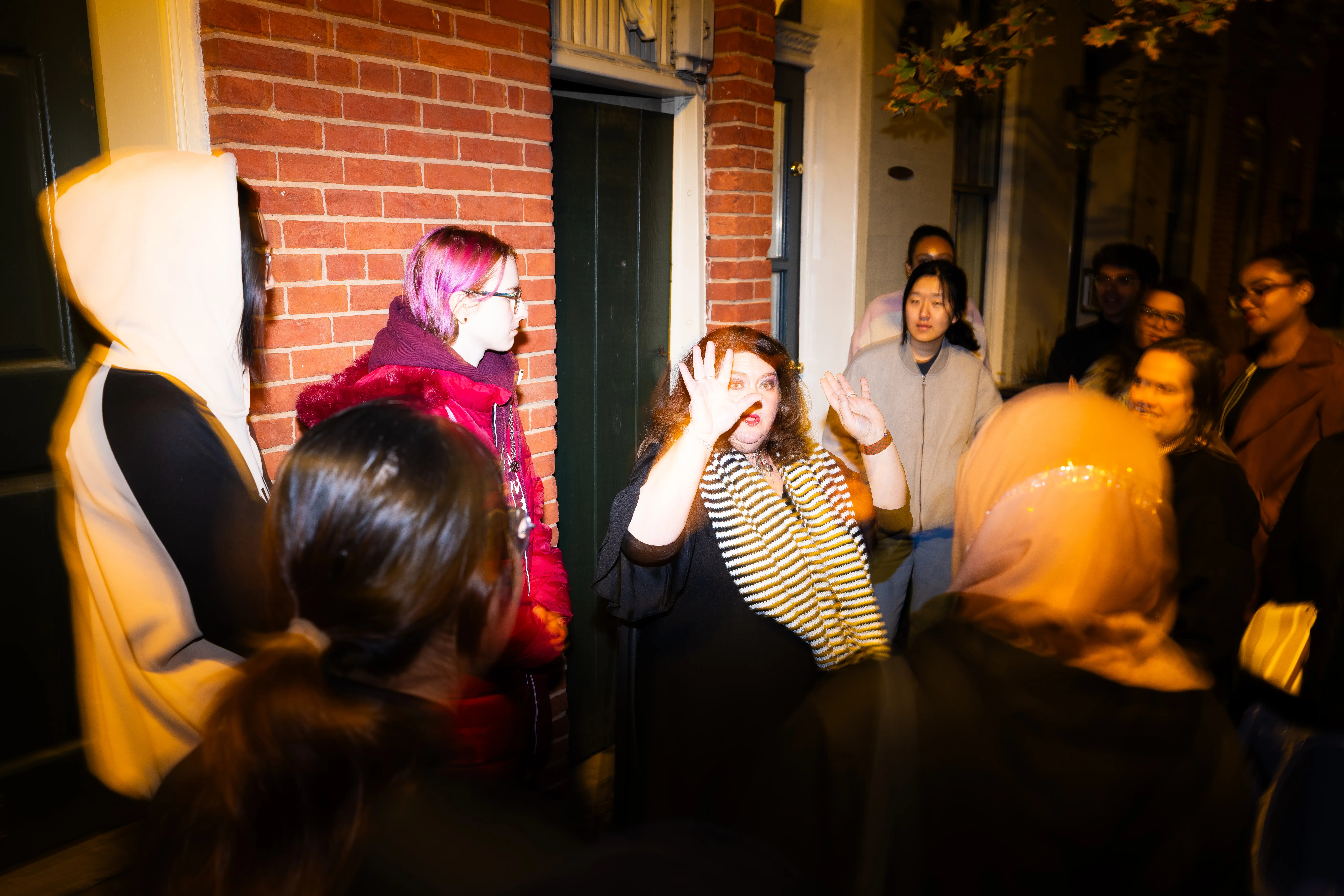 A group gathers at night outside a brick building while one person gestures during a sidewalk discussion.