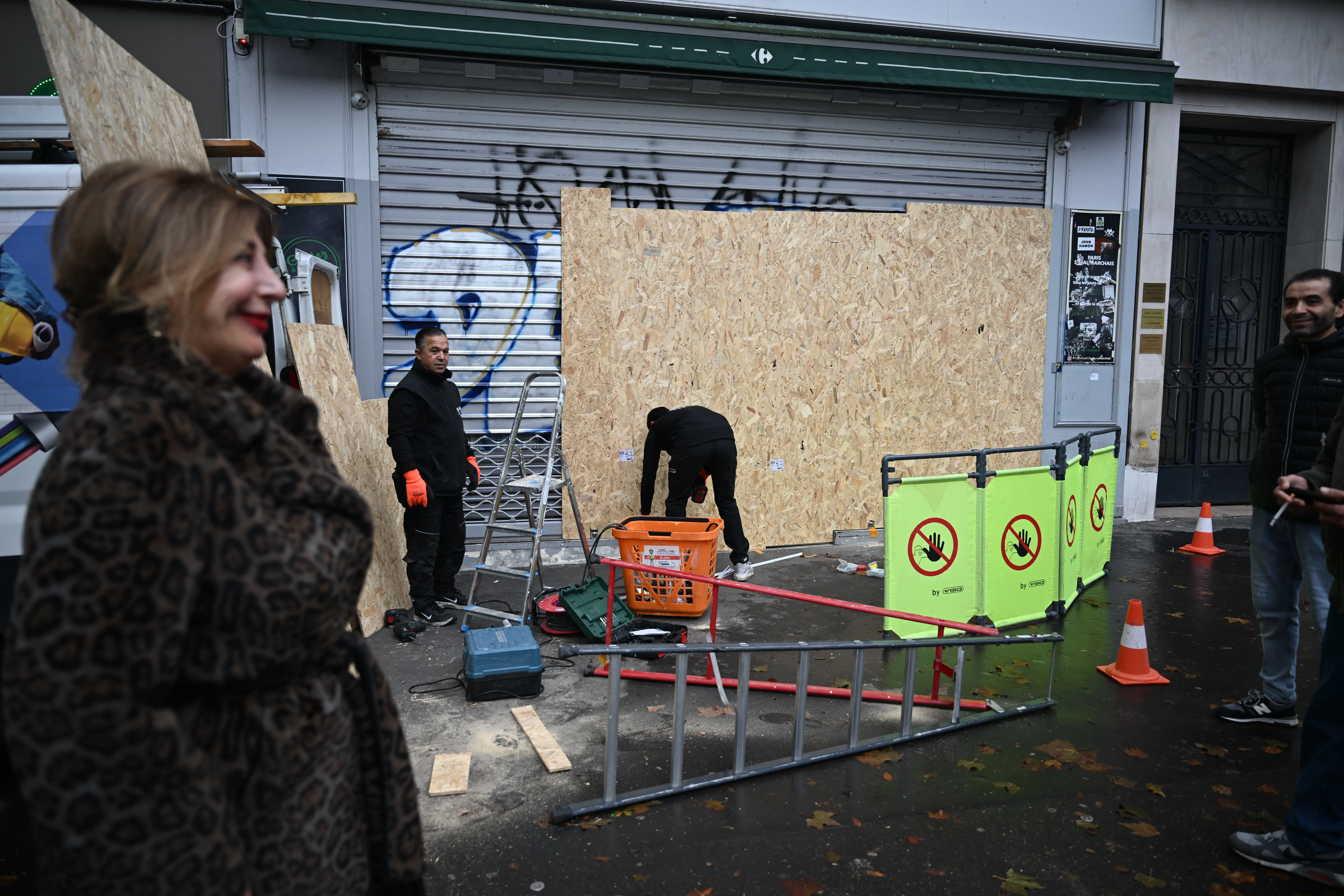 Men board up a store in France as a woman looks on