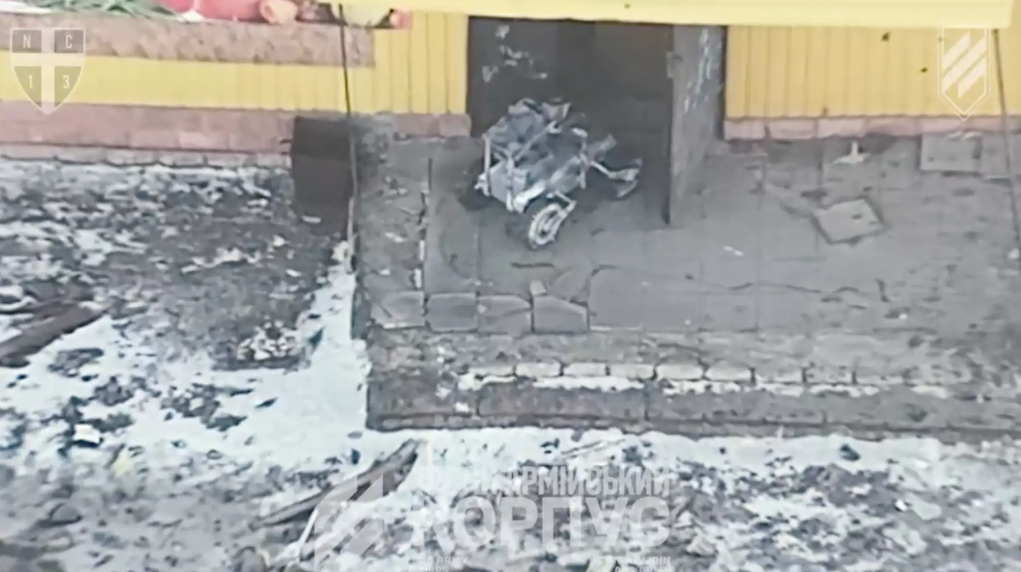 Snow-covered damaged entrance with scattered debris and a wrecked scooter near a yellow building facade.