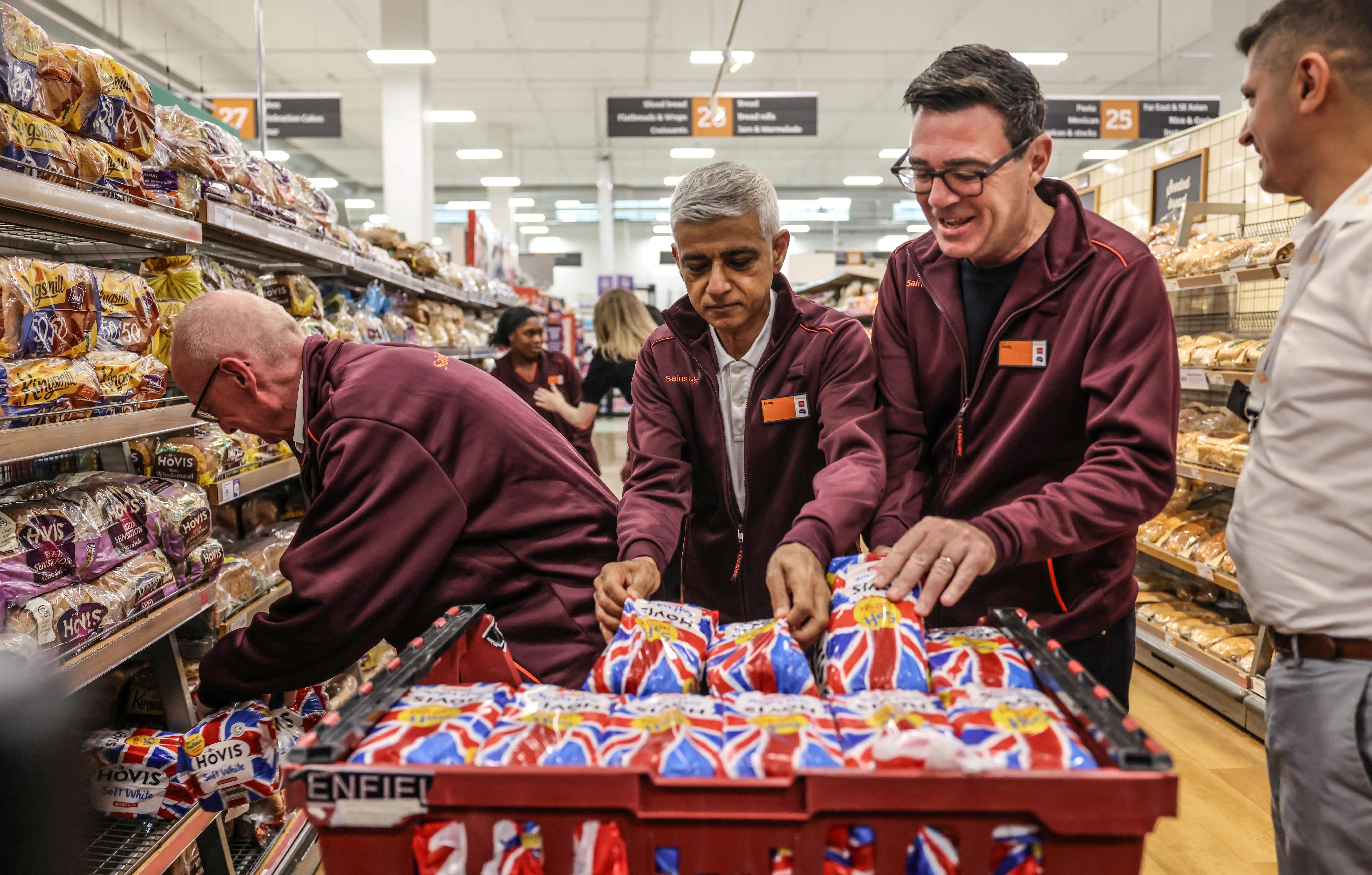 UK Prime Minister Andy Burnham and two ministers stack bread loaves at a supermarket for an event in August.