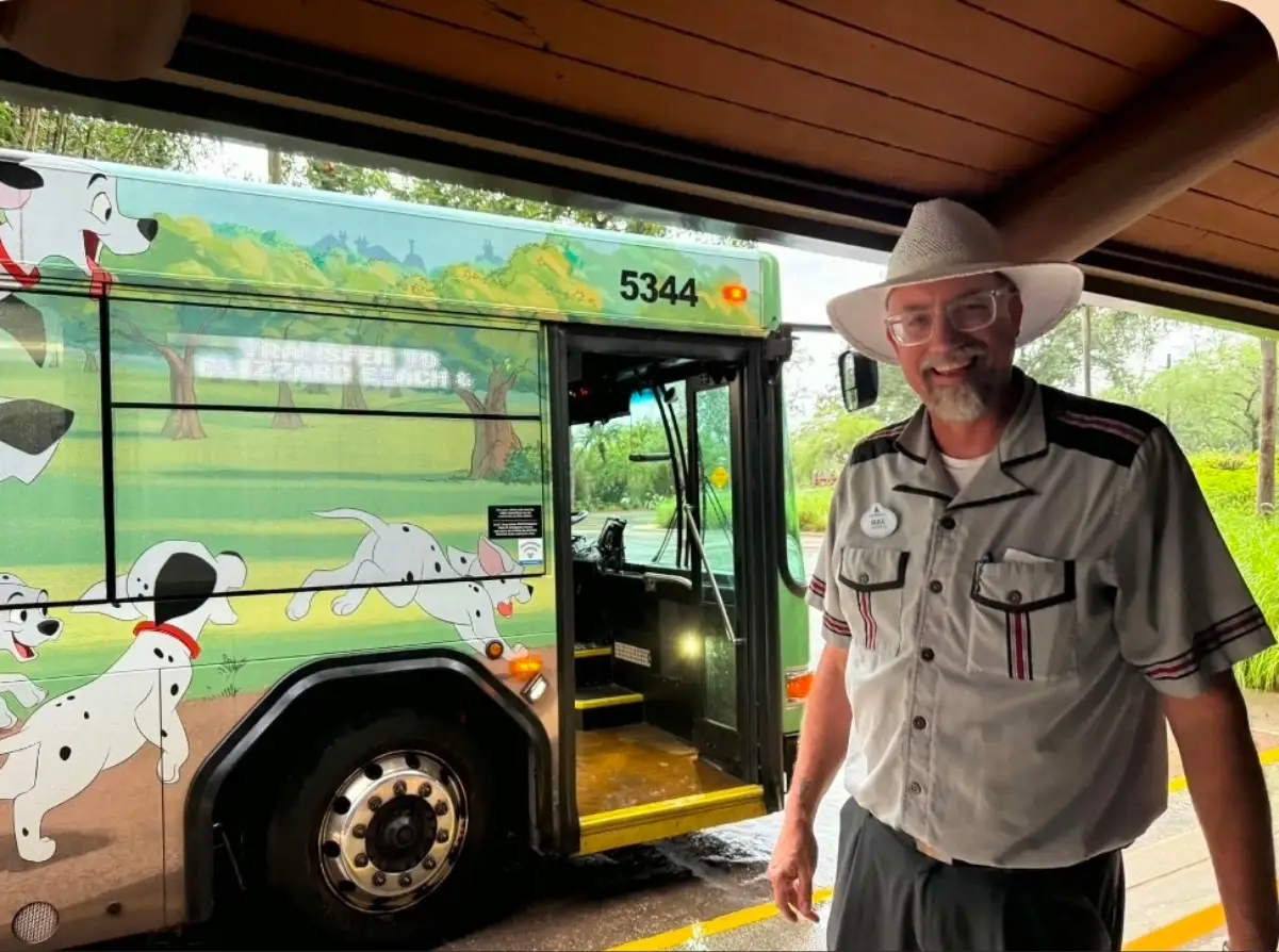 Smiling uniformed person stands beside a Disney bus wrapped with 101 Dalmatians artwork and the number 5344.