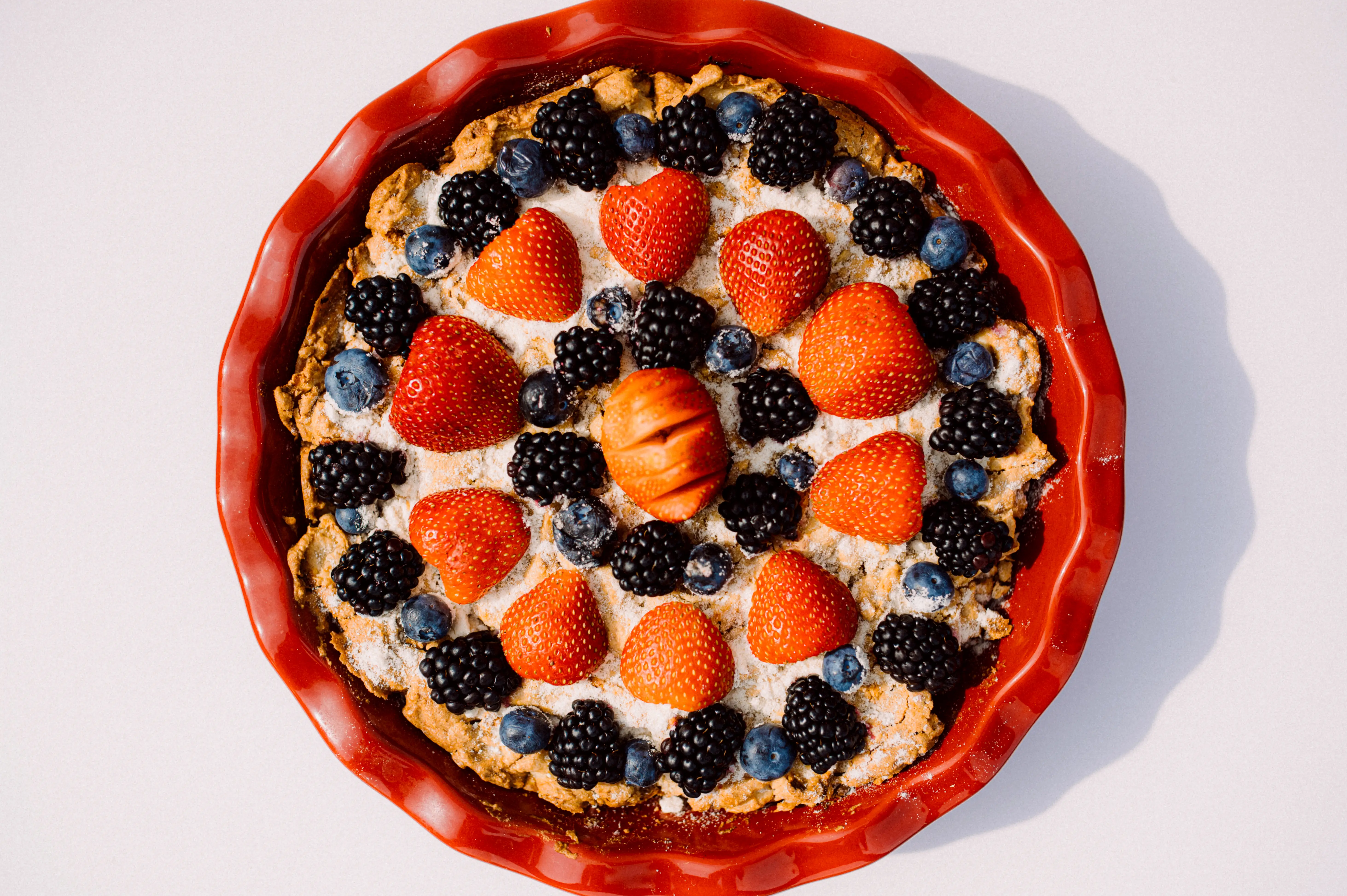 tart is adorned with fresh strawberries, blackberries, and blueberries arranged in a circular pattern.
