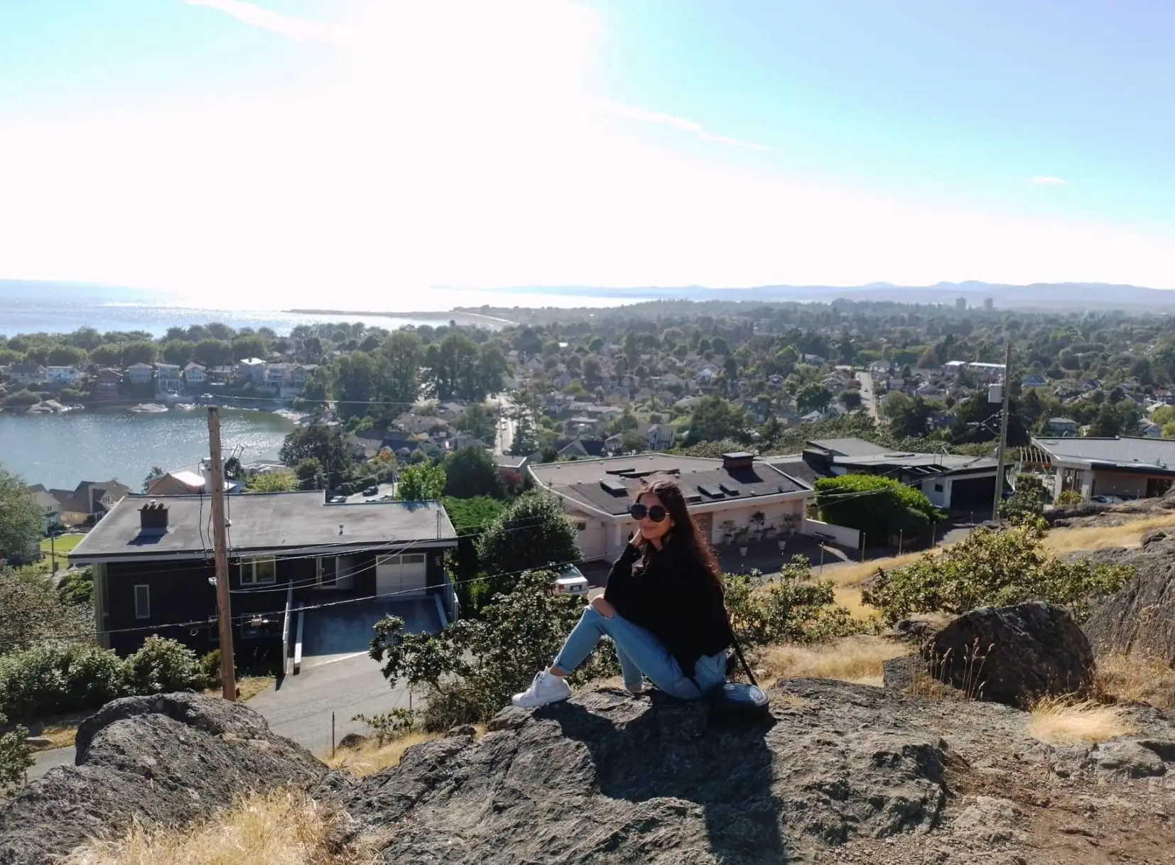 The writer sitting on a mountain overlooking homes in Canada, with a body of water in the background.