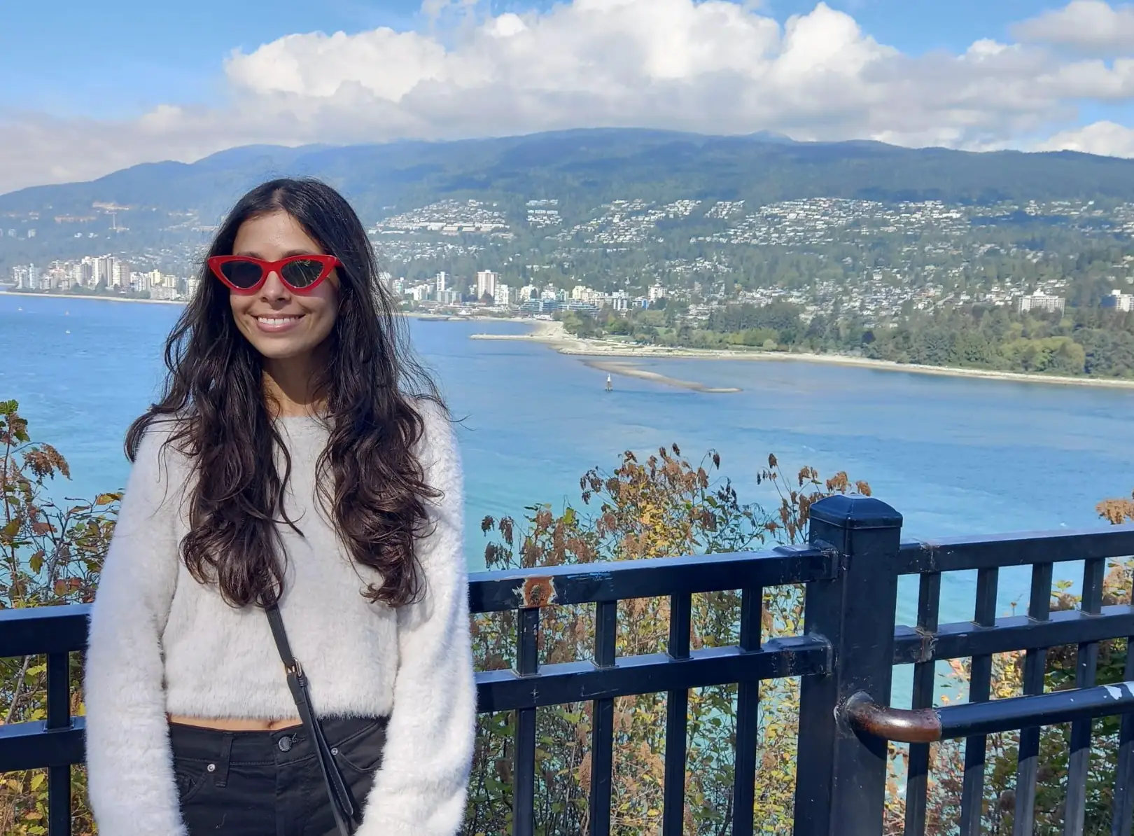 The writer, wearing red sunglasses, stands at a scenic overlook in Canada, with a body of water in the background.