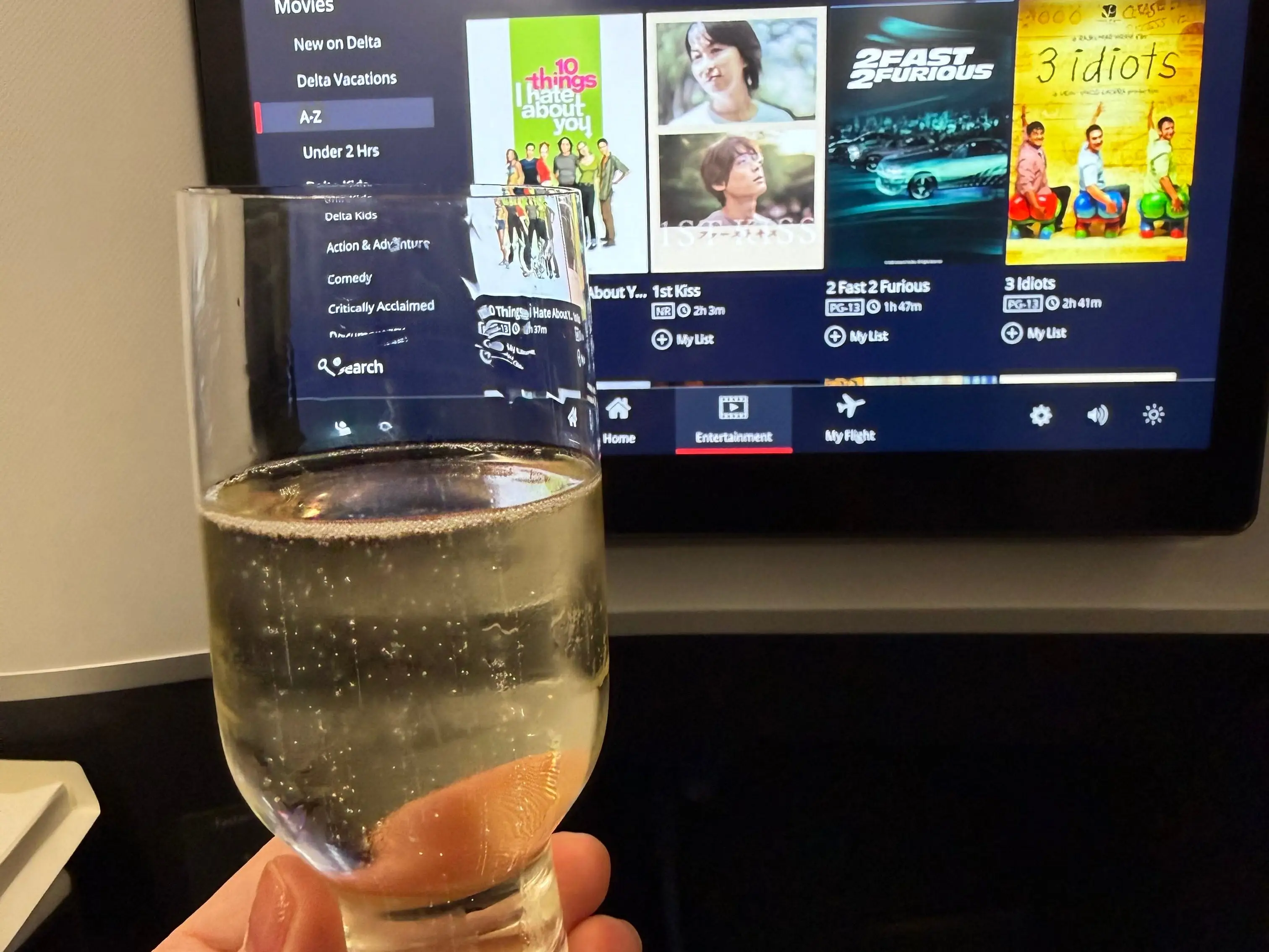 author holding a glass of champagne in front of the inflight tv on delta.