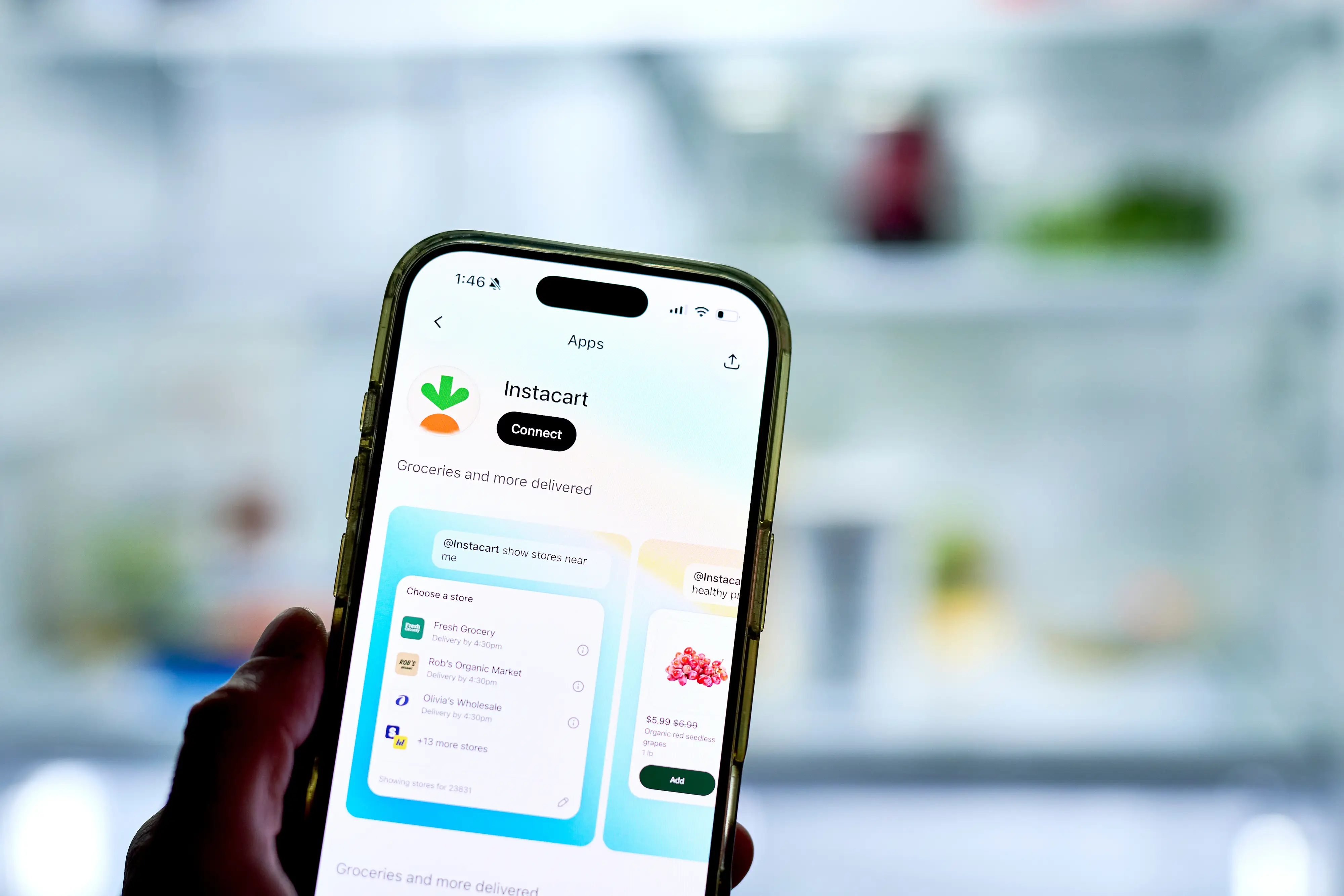 Hand holds a smartphone displaying the Instacart app listing against a blurred refrigerator interior background.