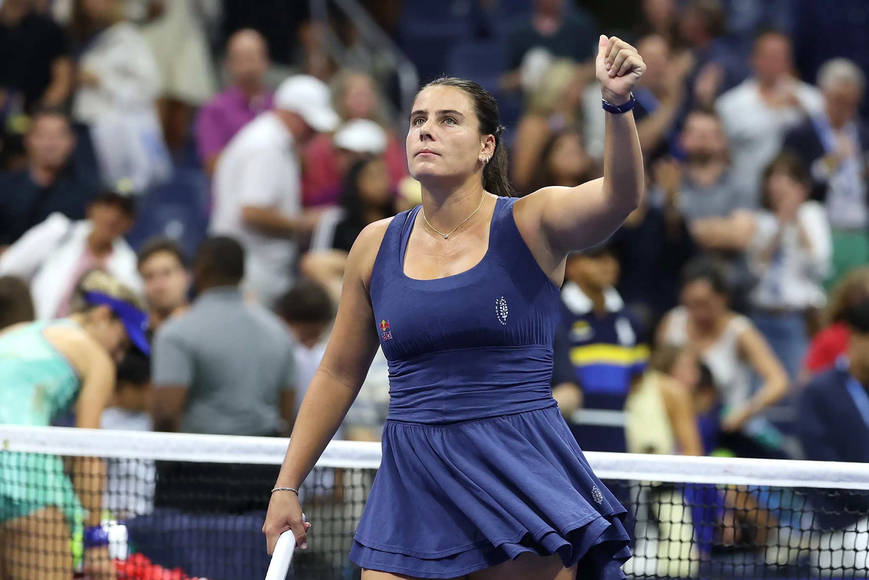 A tennis player in a navy dress raises a fist beside the net on a crowded stadium court.