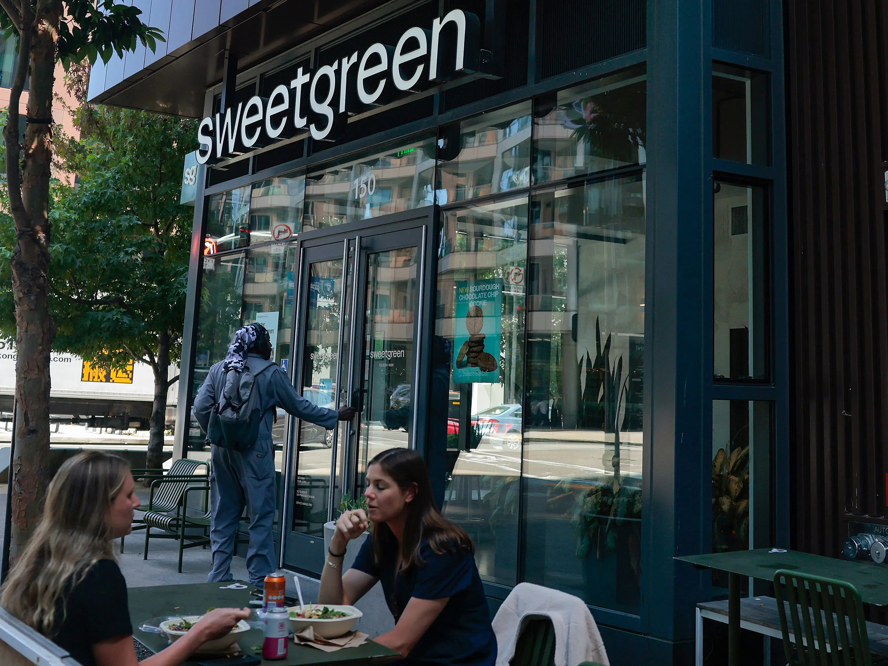 Sweetgreen storefront with sidewalk dining tables and several patrons seated outside on a city street.